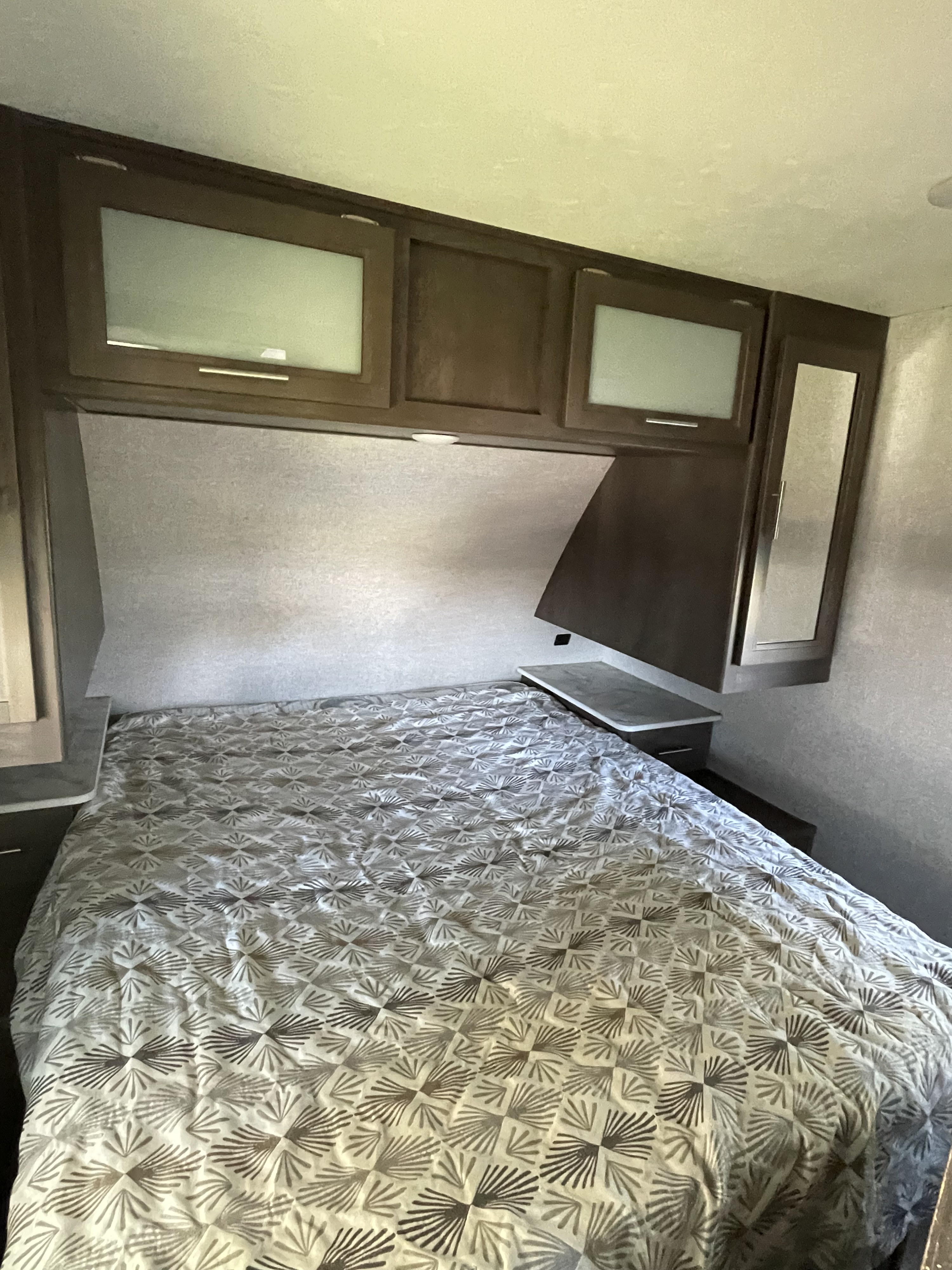 Cozy RV rental bedroom featuring a bed with patterned comforter, overhead cabinets, and built-in nightstands for comfort on the road.. Dutchmen Coleman Light 2021