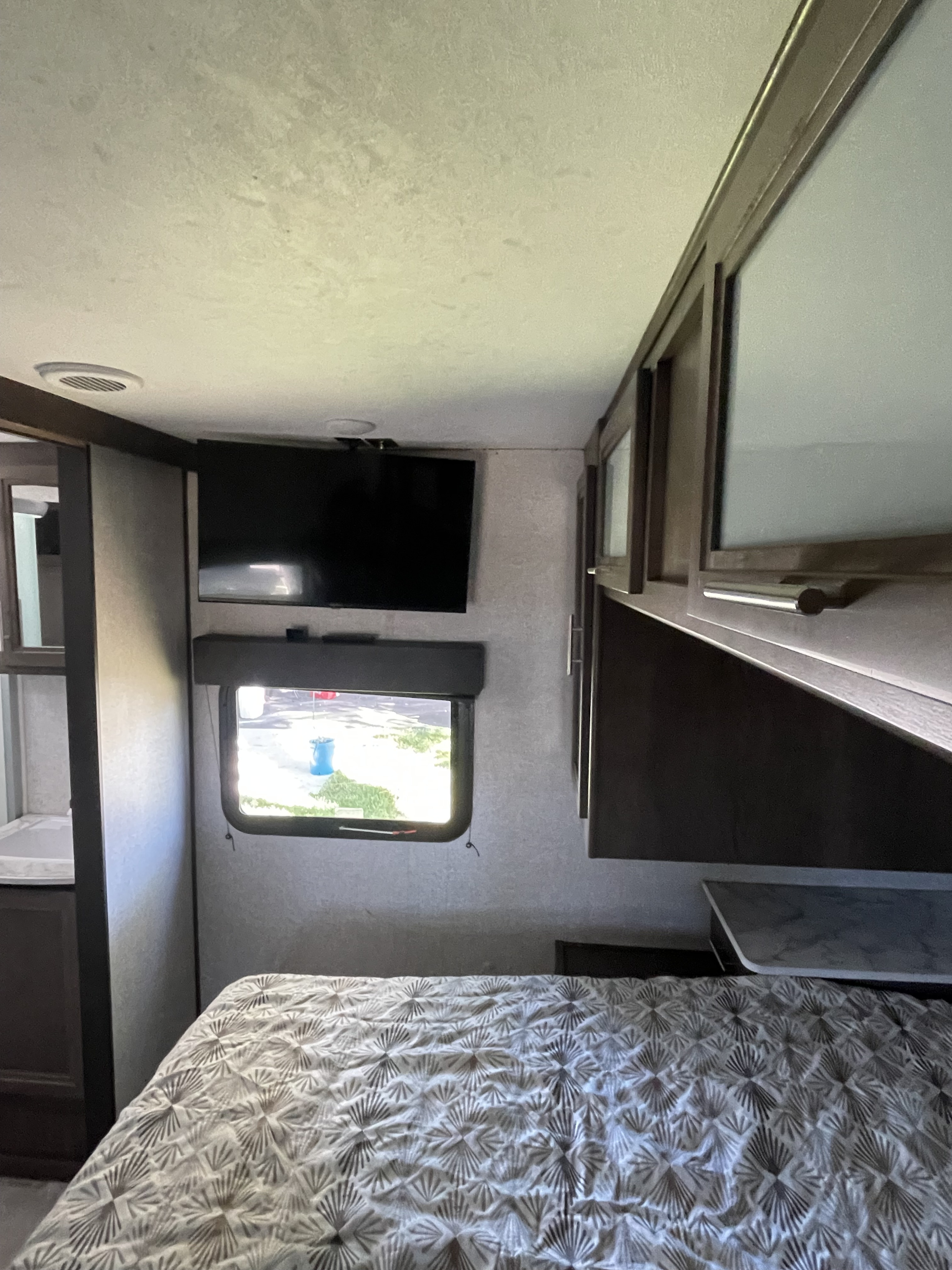 Explore this RV rental bedroom interior: a comfy bed, wall-mounted TV, window with blind, and overhead cabinets.. Dutchmen Coleman Light 2021