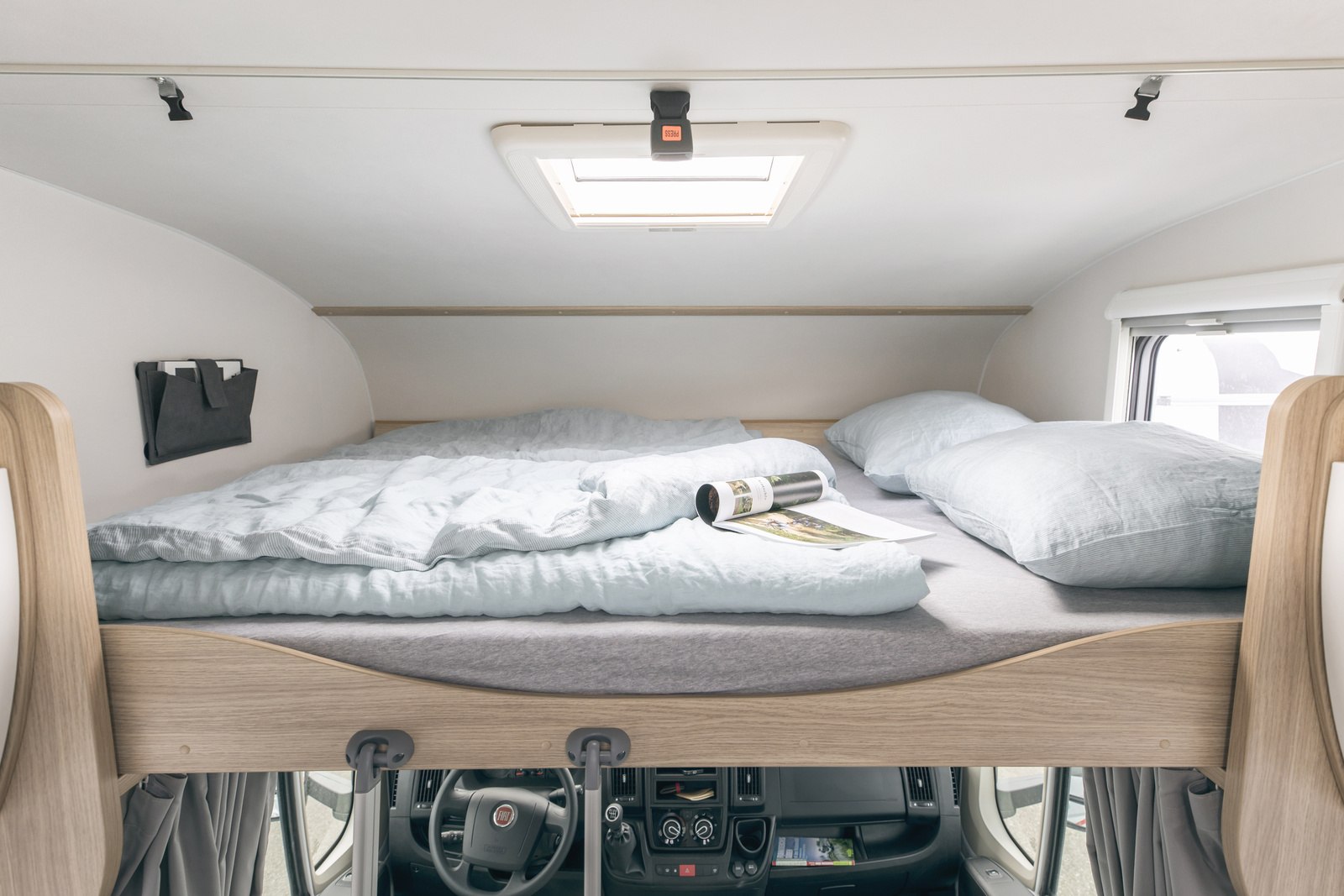 Relaxing over-cab bed in an **rv rental**, showing light blue bedding, pillows, and a ceiling skylight above the driver's cabin.. Sunlight A70 2026