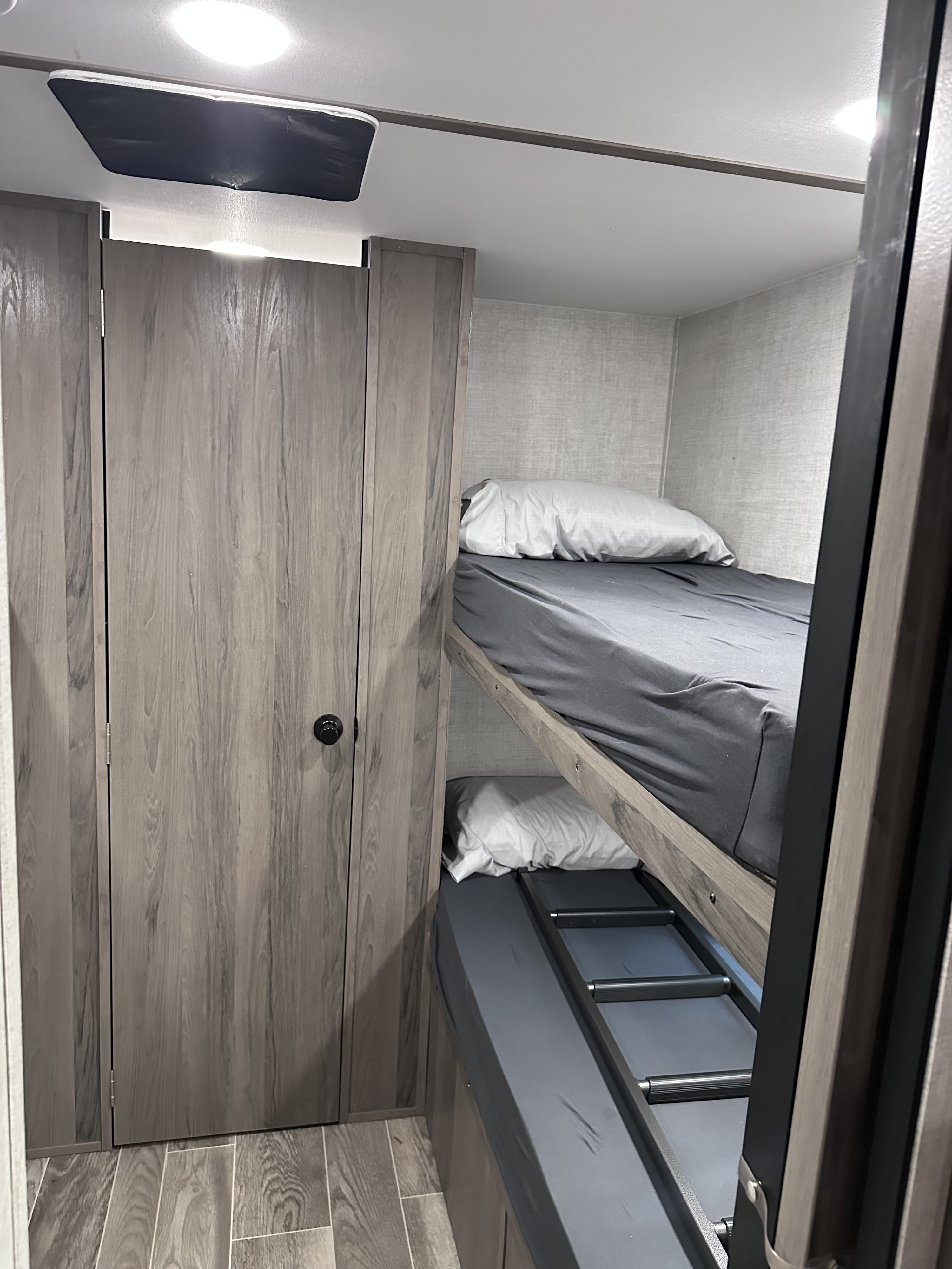 Compact RV rental bunk beds with dark sheets, white pillows, and modern wood cabinets create a cozy sleeping area.. Gulf Stream Ameri-Lite 2022