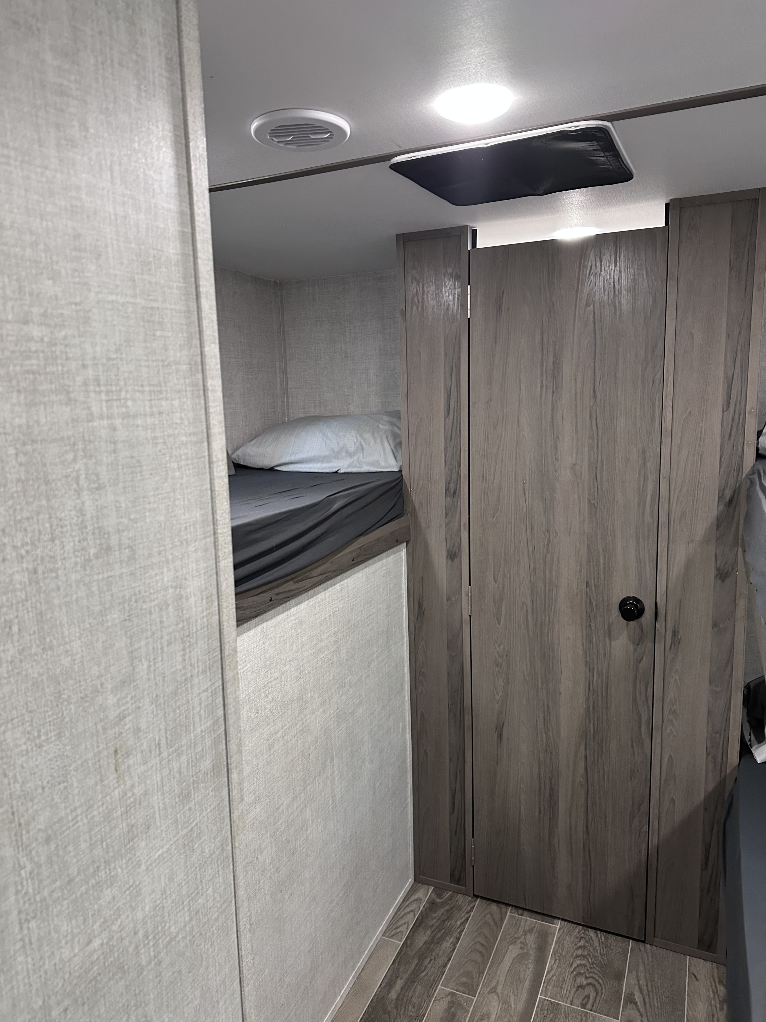 View inside an RV rental showing a bunk bed with gray bedding, an adjacent wood-grain closet, and ceiling details.. Gulf Stream Ameri-Lite 2022