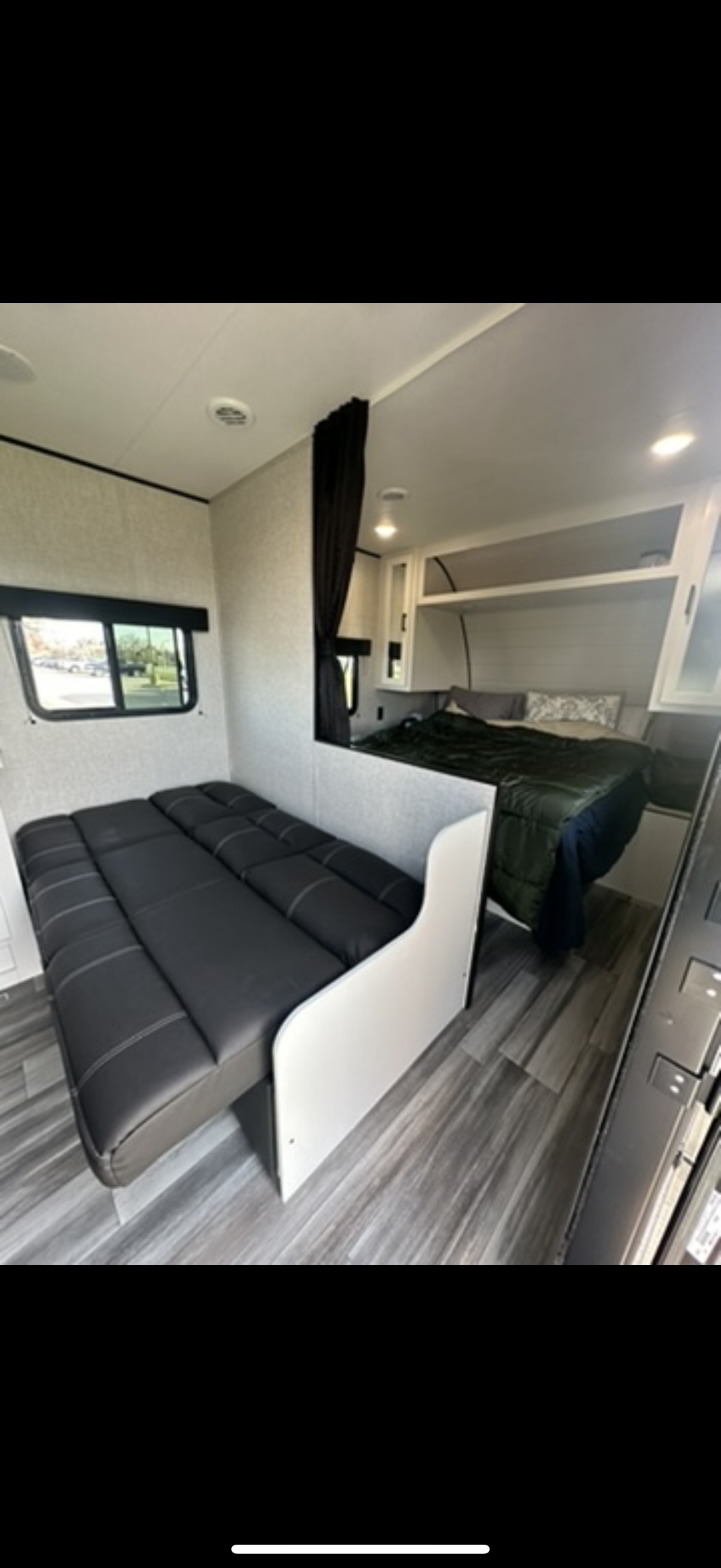 This RV rental interior features a cozy bed with green bedding behind a partition, next to a black cushioned sofa.. Jayco Jay Flight SLX 2024