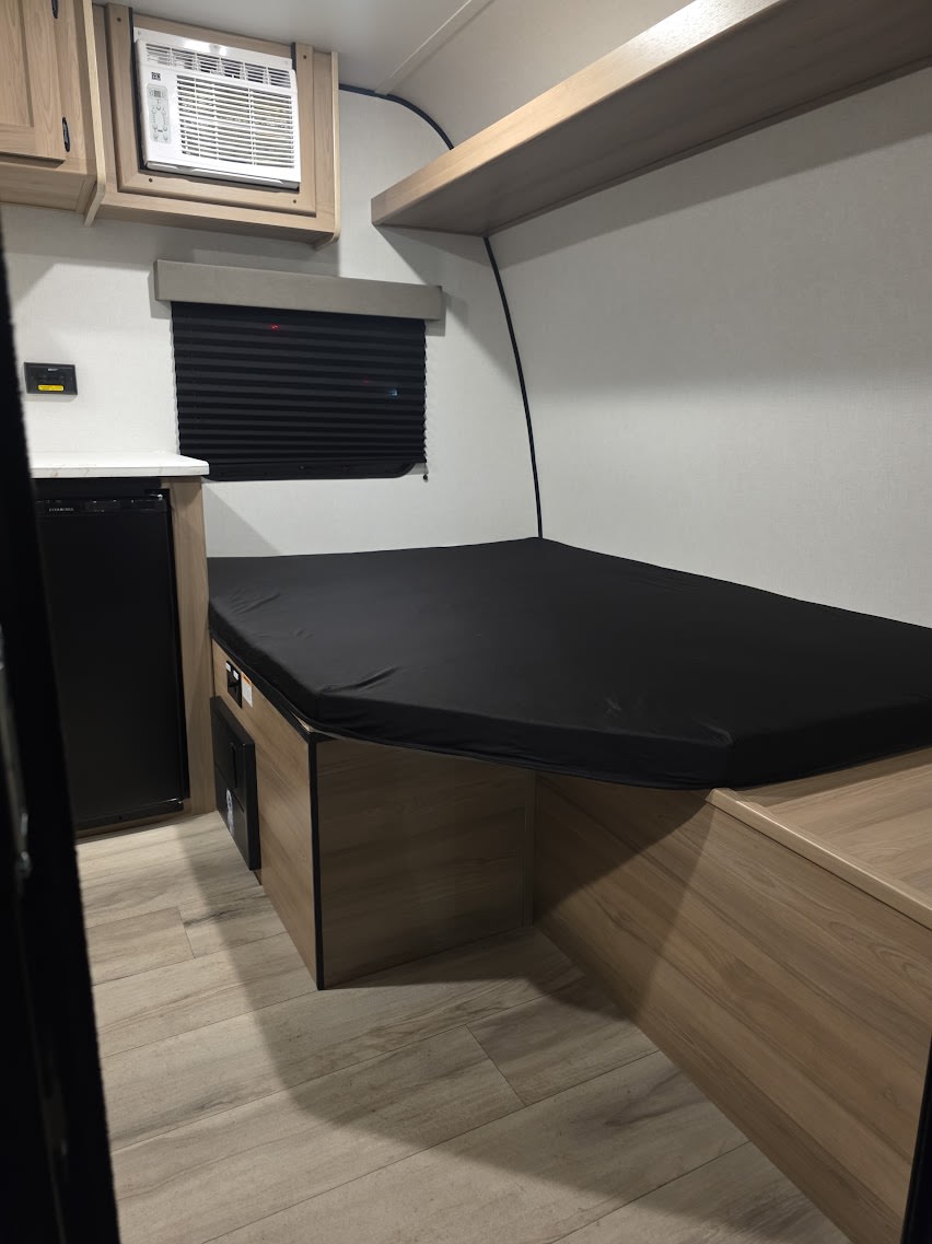 Compact rv rental interior features a cozy bed, mini-fridge, AC, and wood-look flooring.. KEYSTONE COLEMAN 13B 2026