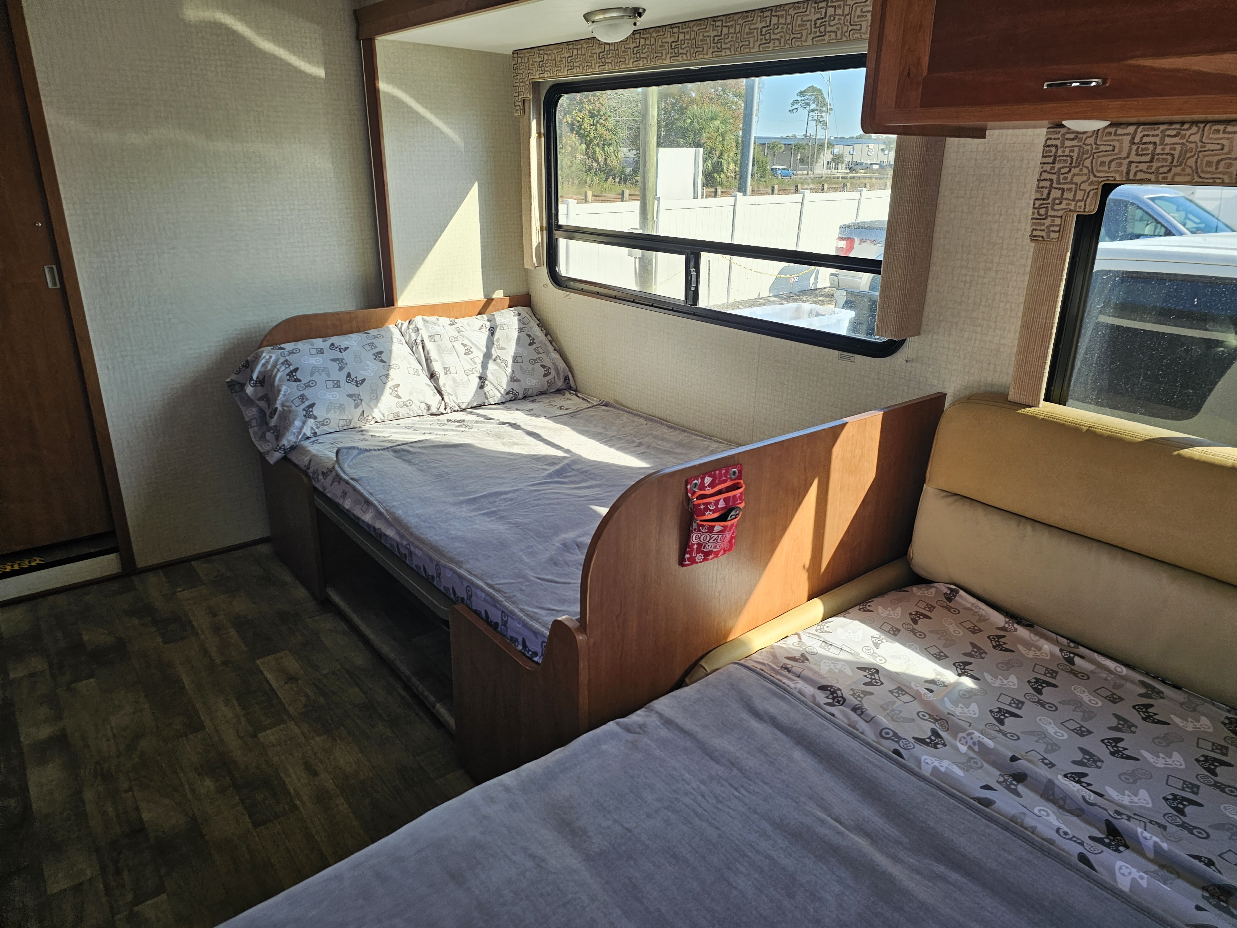 Cozy RV rental interior featuring bunk beds with patterned sheets, bright window views, and warm sunlight.. Winnebago Spirit 2018