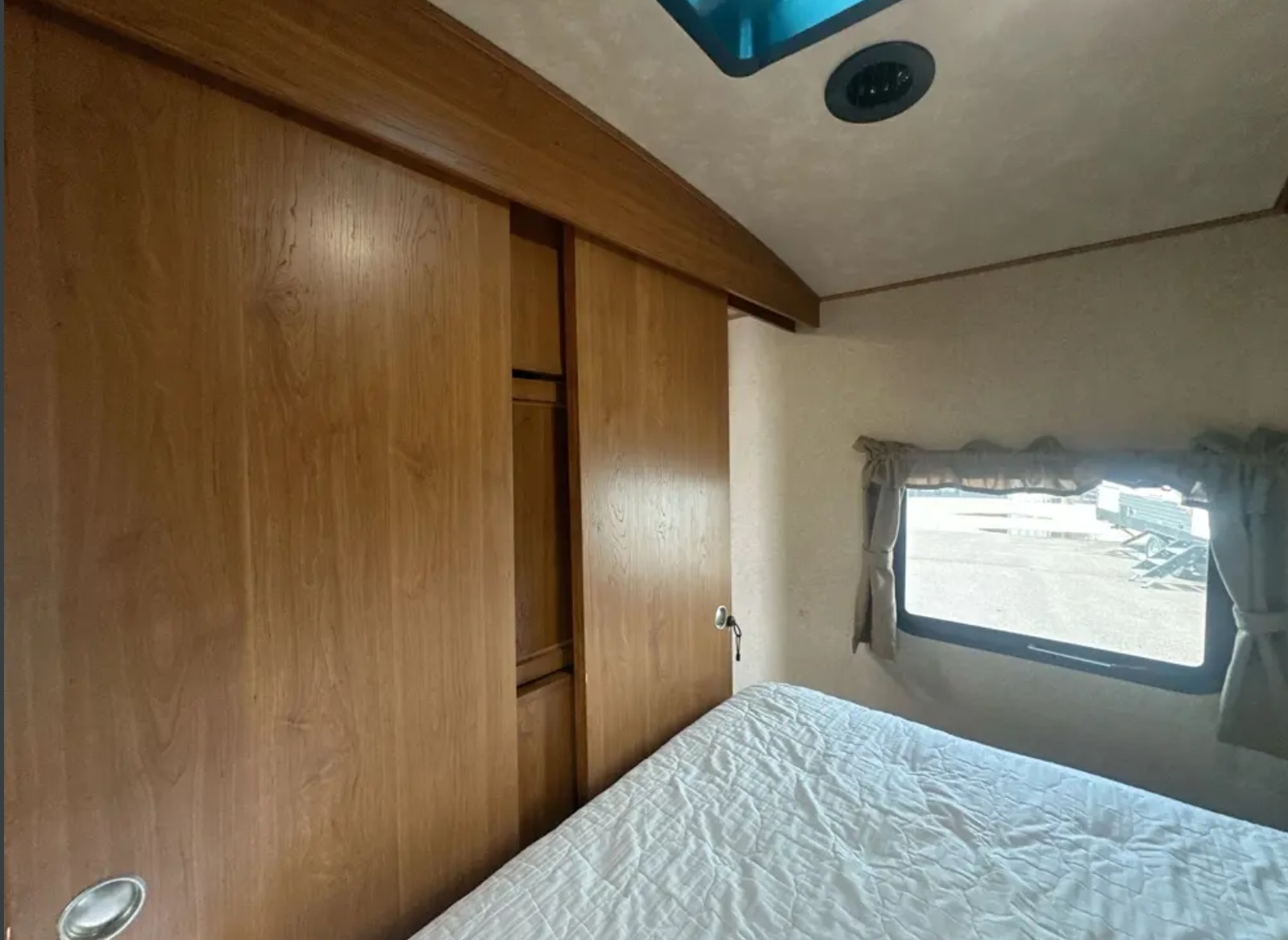 RV rental bedroom interior featuring wood-paneled sliding doors, a comfortable bed with white bedding, and a window.. Crossroads RV Sunset Trail Super Lite 2017