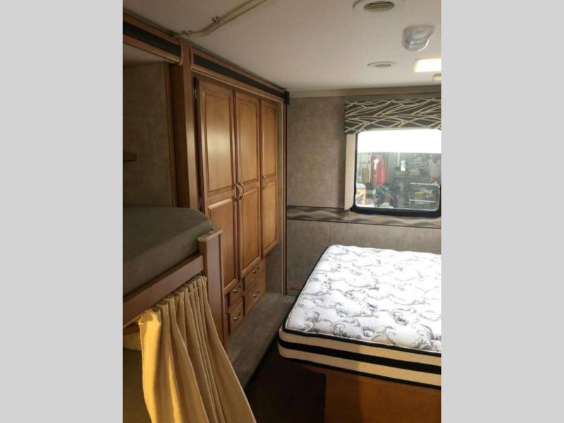 RV rental bedroom interior featuring a main bed, bunk beds with privacy curtain, and a wooden wardrobe for storage.. Winnebago MINNIE WINNIE 31H 2016