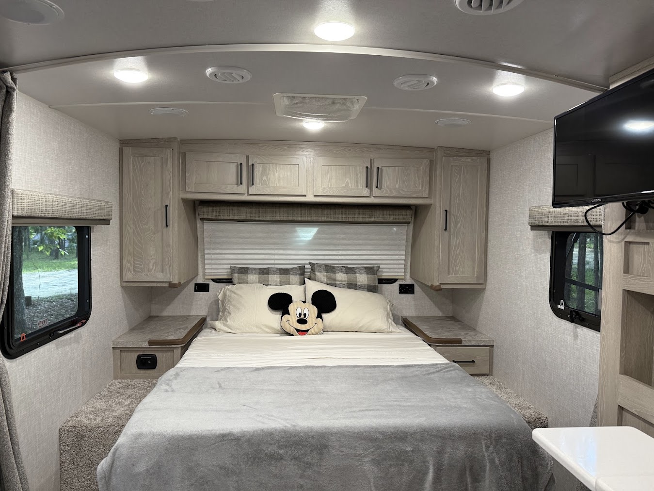 Cozy rv rental bedroom interior: light decor, comfy bed with Mickey Mouse pillow, storage, TV, and side windows.. Forest River Flagstaff Micro Lite 2022