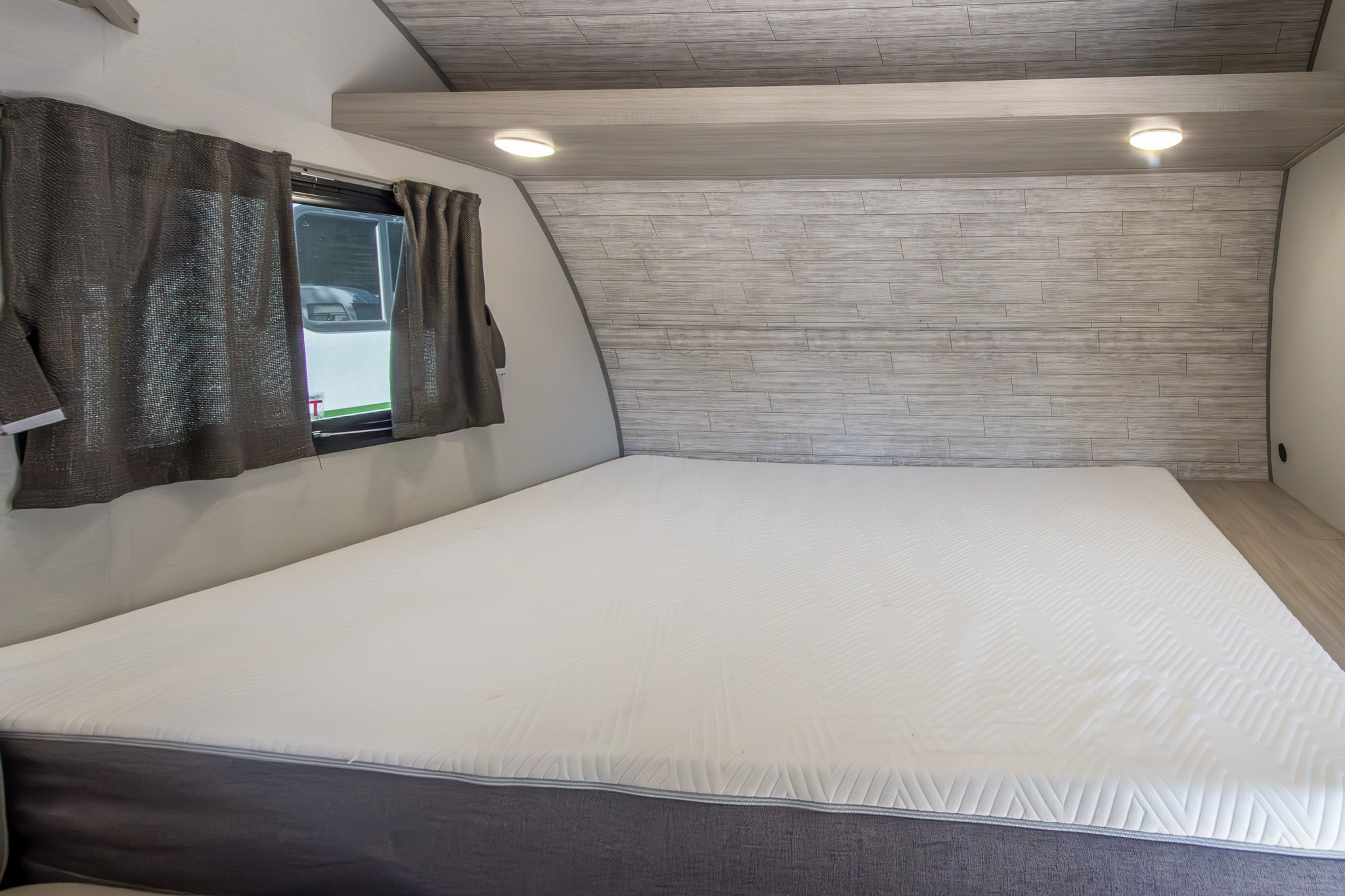 Inside an RV rental: a comfortable bedroom featuring a large mattress, window, and modern wood-look headboard with lighting.. Coachmen Other 2024