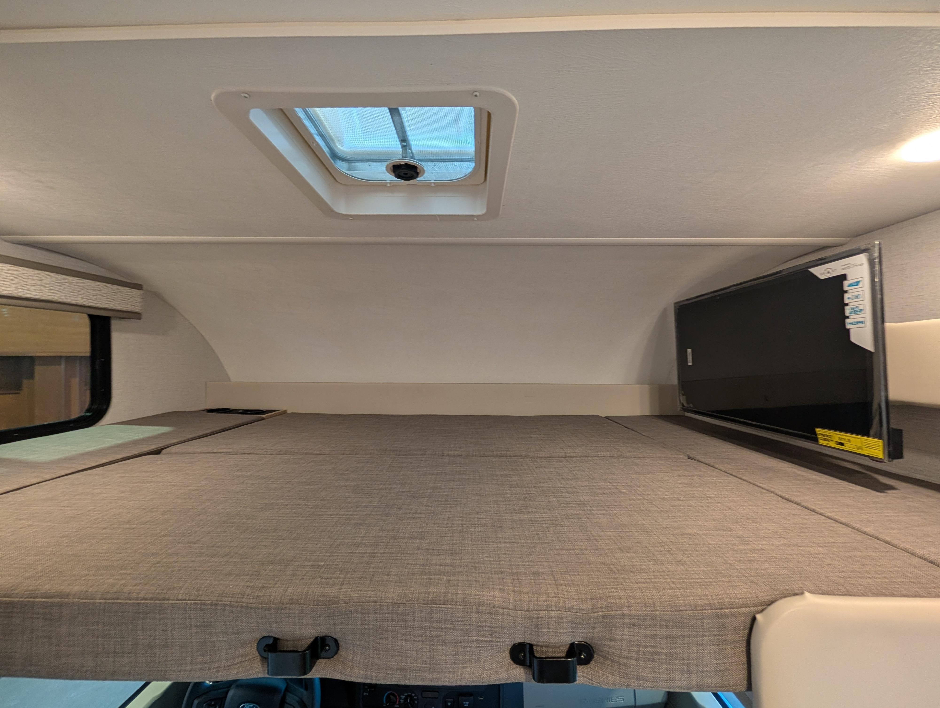 Spacious rv rental cab-over bunk with comfy mattress, a bright skylight, side window, and mounted TV.. Thor Chateau 2026