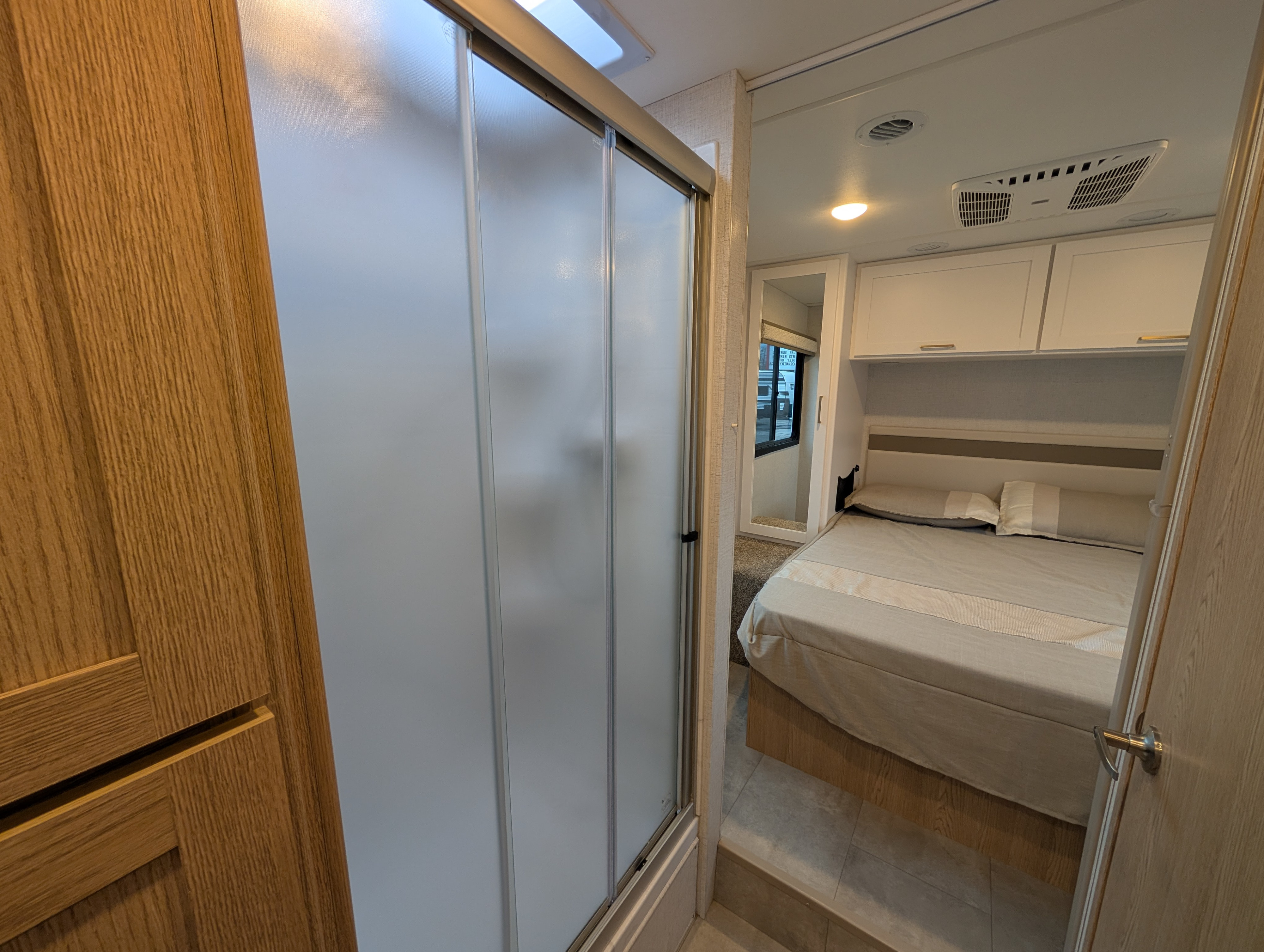 Inside an RV rental, showing a bedroom with a bed and cabinets, viewed past a frosted glass shower door.. THOR CHATEAU 2026