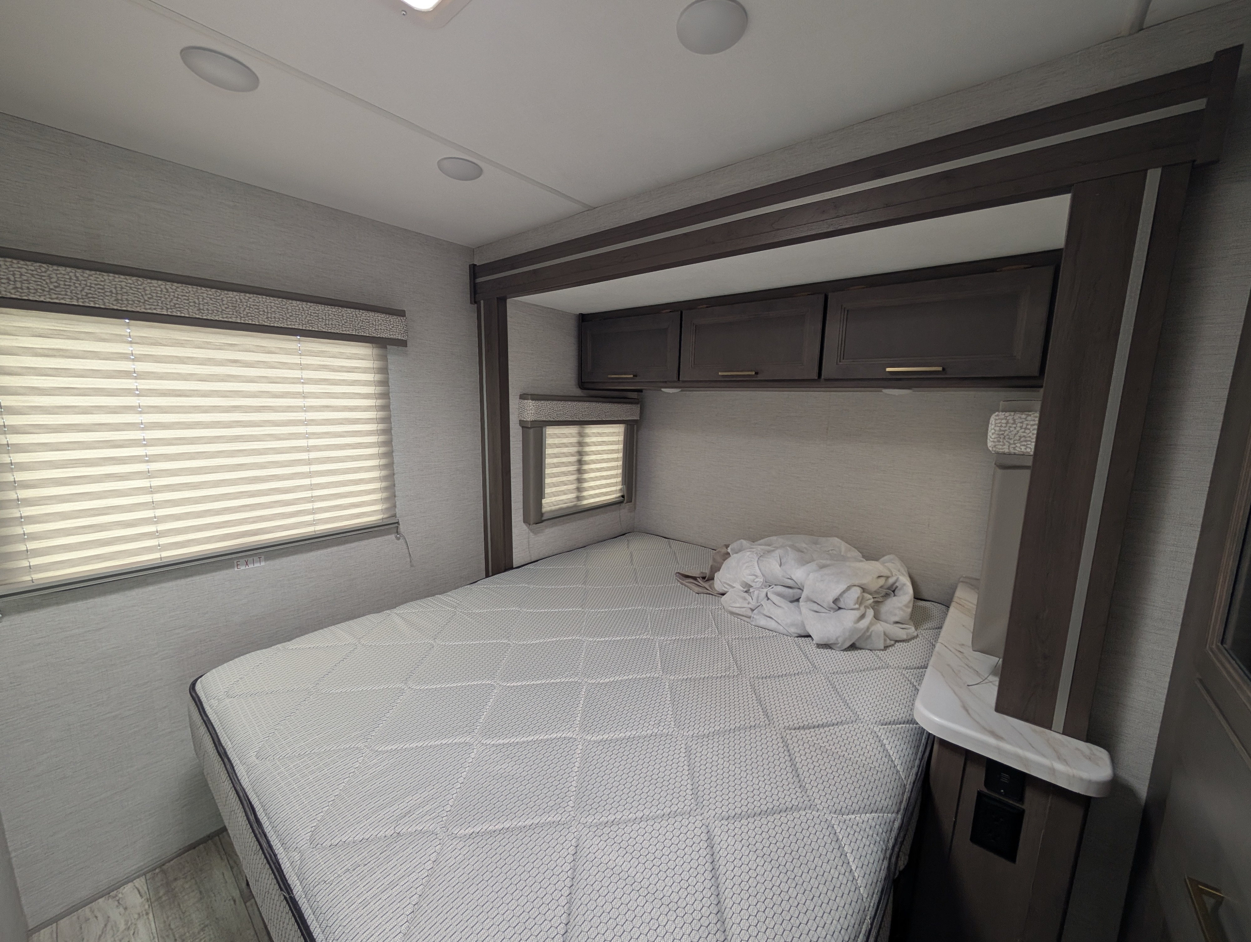 RV rental bedroom interior, featuring a comfortable bed, overhead cabinets, and windows with blinds, ideal for travel.. Thor Chateau 2026