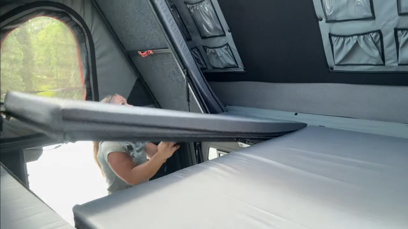 Cozy RV rental setup: Woman adjusts mattress inside camper, featuring organized storage & scenic window view for travel.. Toyota Tundra 2019