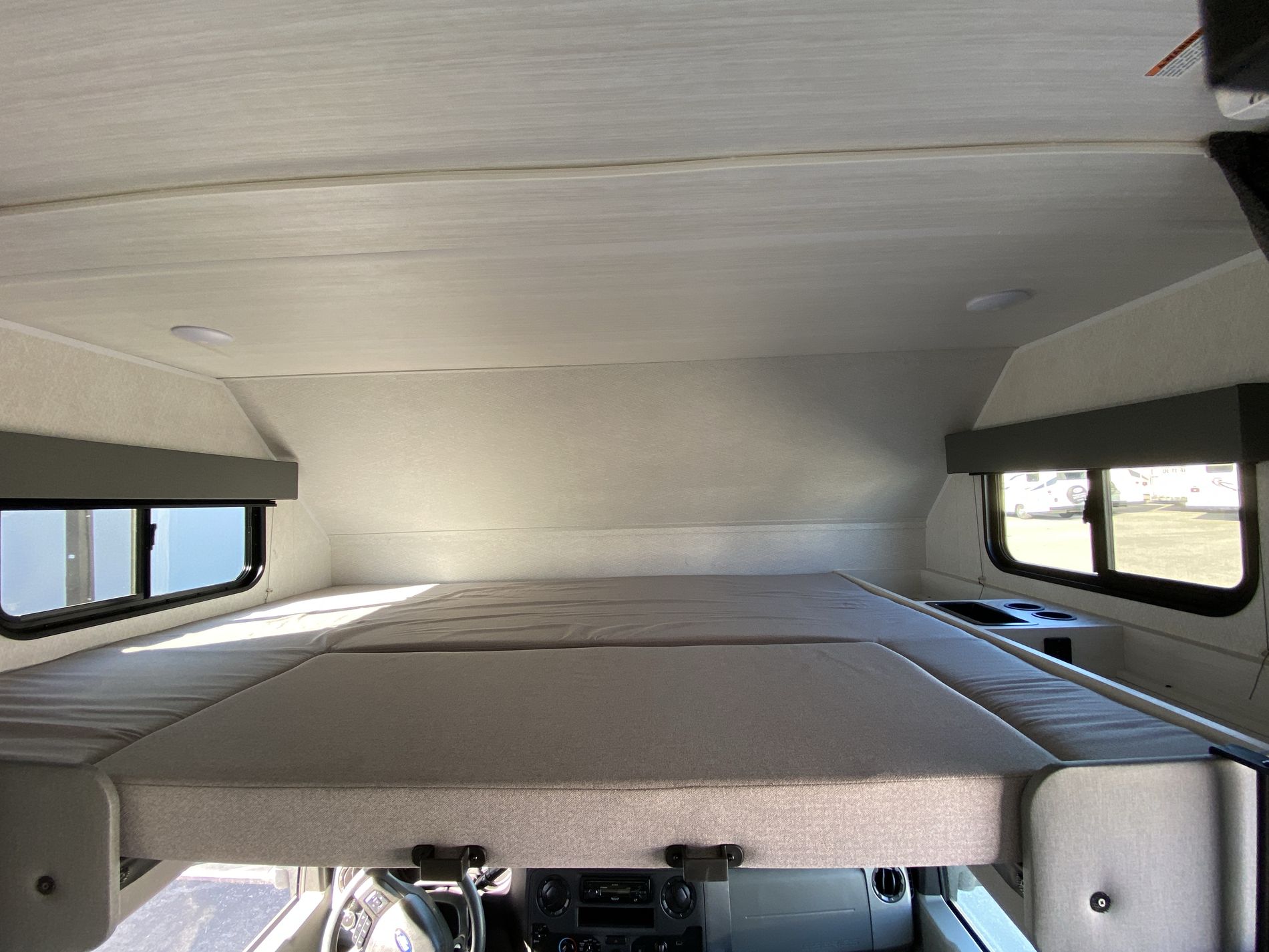 RV rental over-cab bunk bed. Comfortable motorhome sleeping area with side windows and overhead lighting.. East to West Entrada 2024