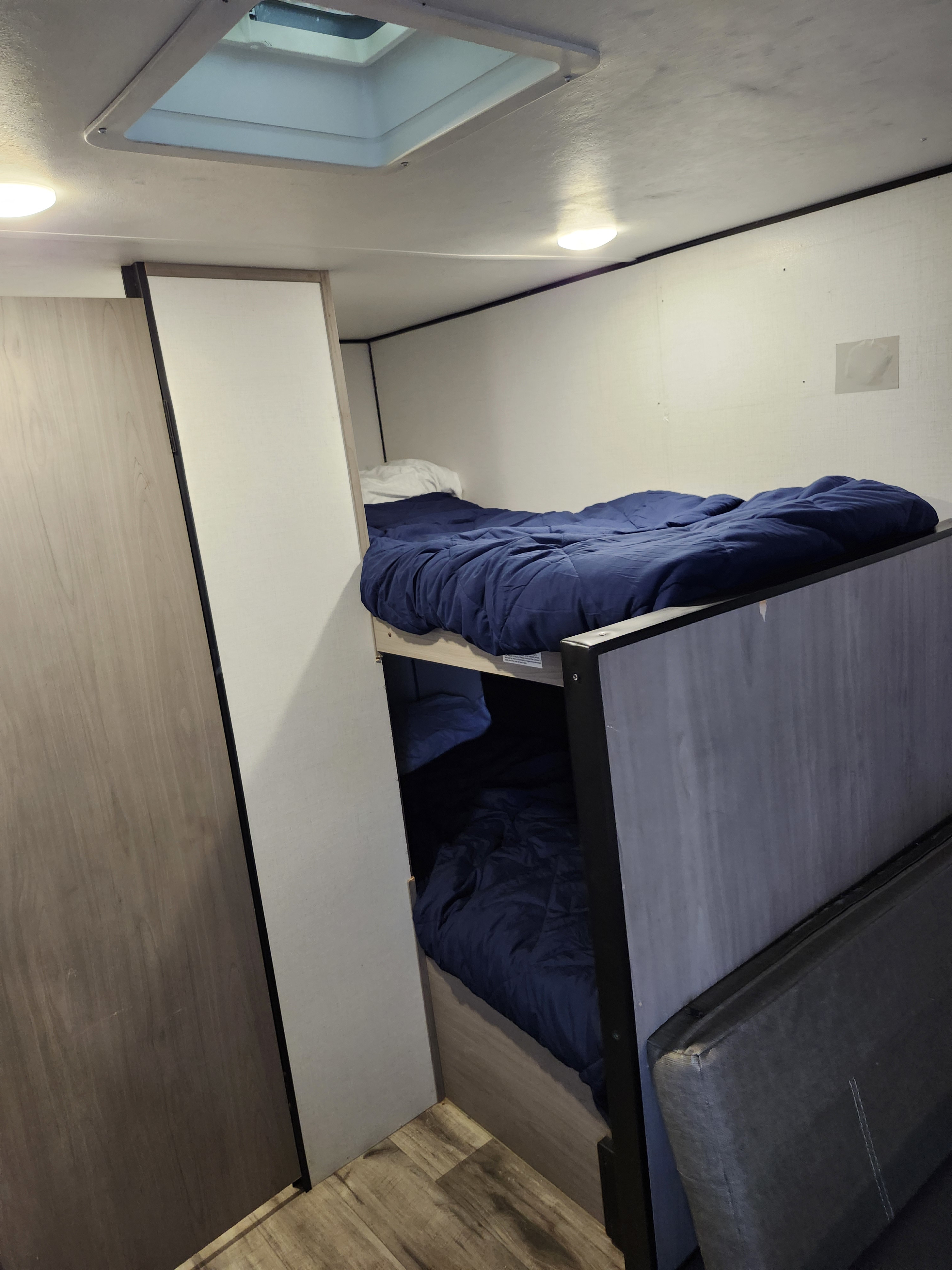 RV rental interior: two cozy bunk beds with blue bedding, an adjacent light wood closet, and a ceiling skylight for light.. Dutchmen Coleman 2024