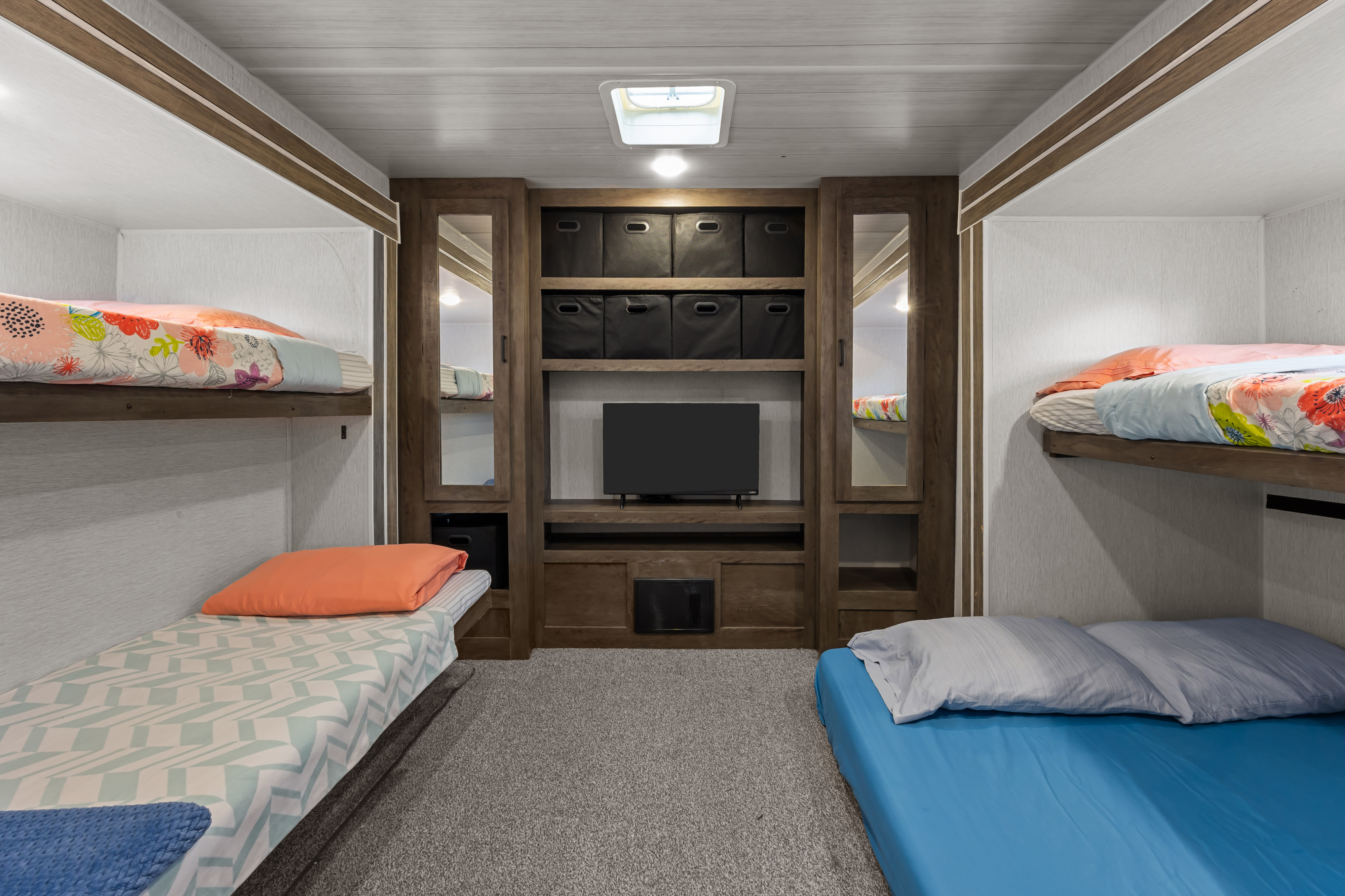 Spacious RV rental bunk room featuring four beds, central TV, and storage, ideal for family adventures in a travel trailer.. Forest River Wildwood 2022