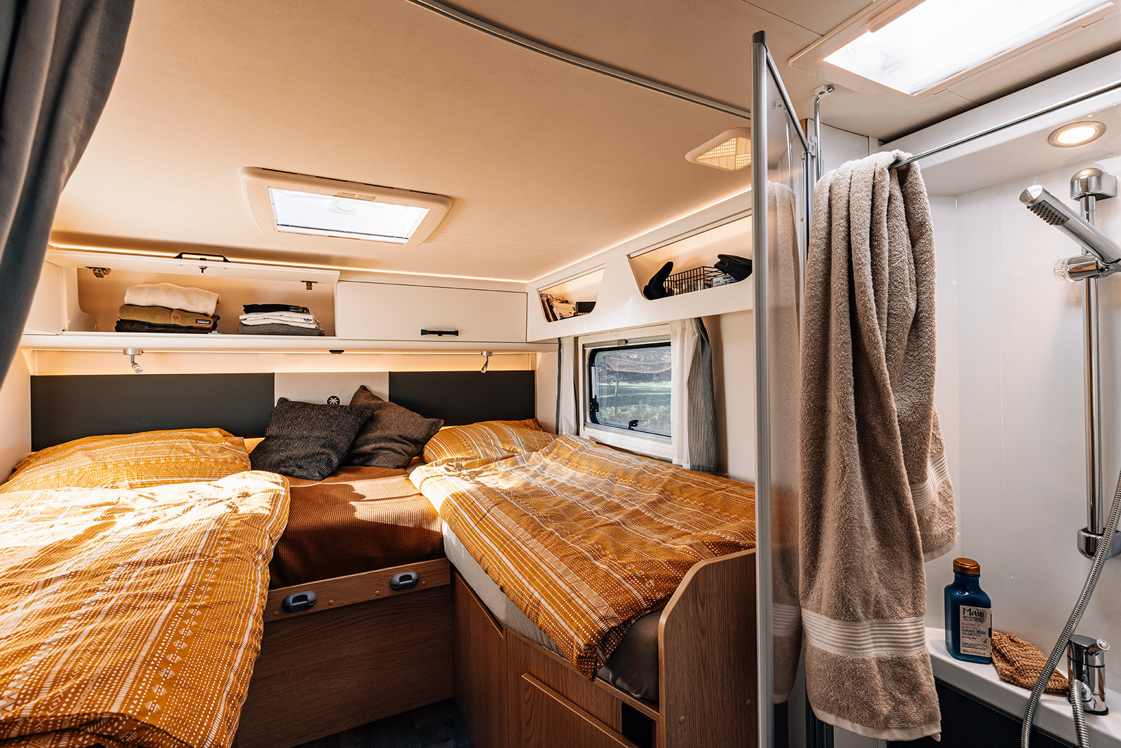 This RV rental interior features a cozy bedroom with patterned bedding, overhead storage, and a compact shower area.. Sunlight I68 2026