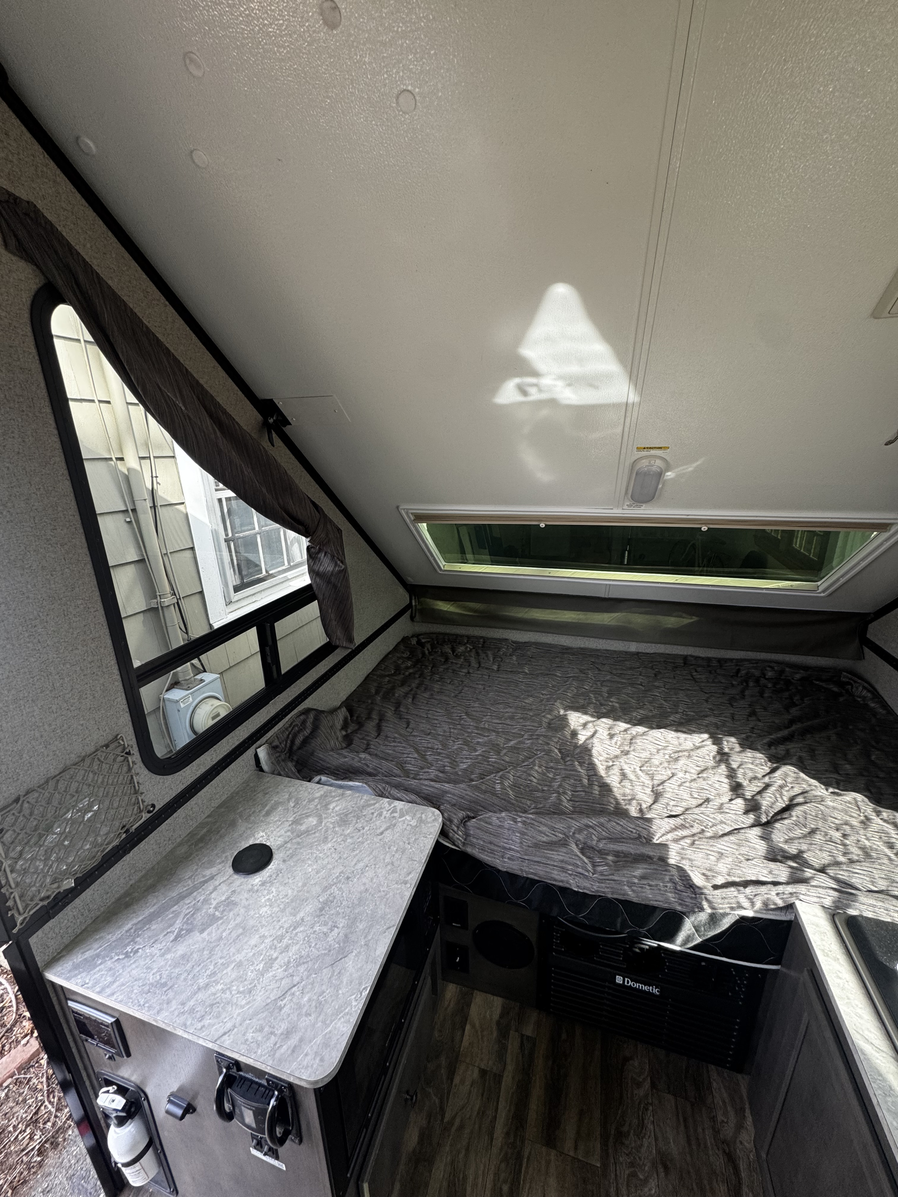 View inside an rv rental: a compact camper features a bed, small counter with a fire extinguisher, Dometic unit, and a window.. Forest River Rockwood Premier 2019