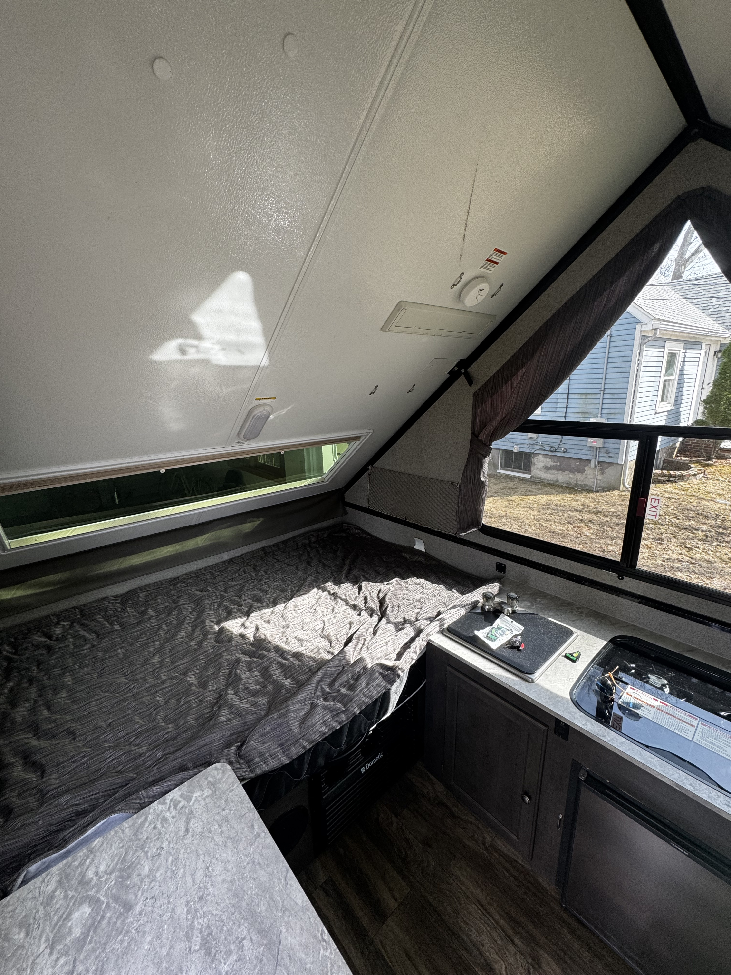 A cozy A-frame RV rental interior features a bed, compact kitchen area, and angular ceiling with windows.. Forest River Rockwood Premier 2019