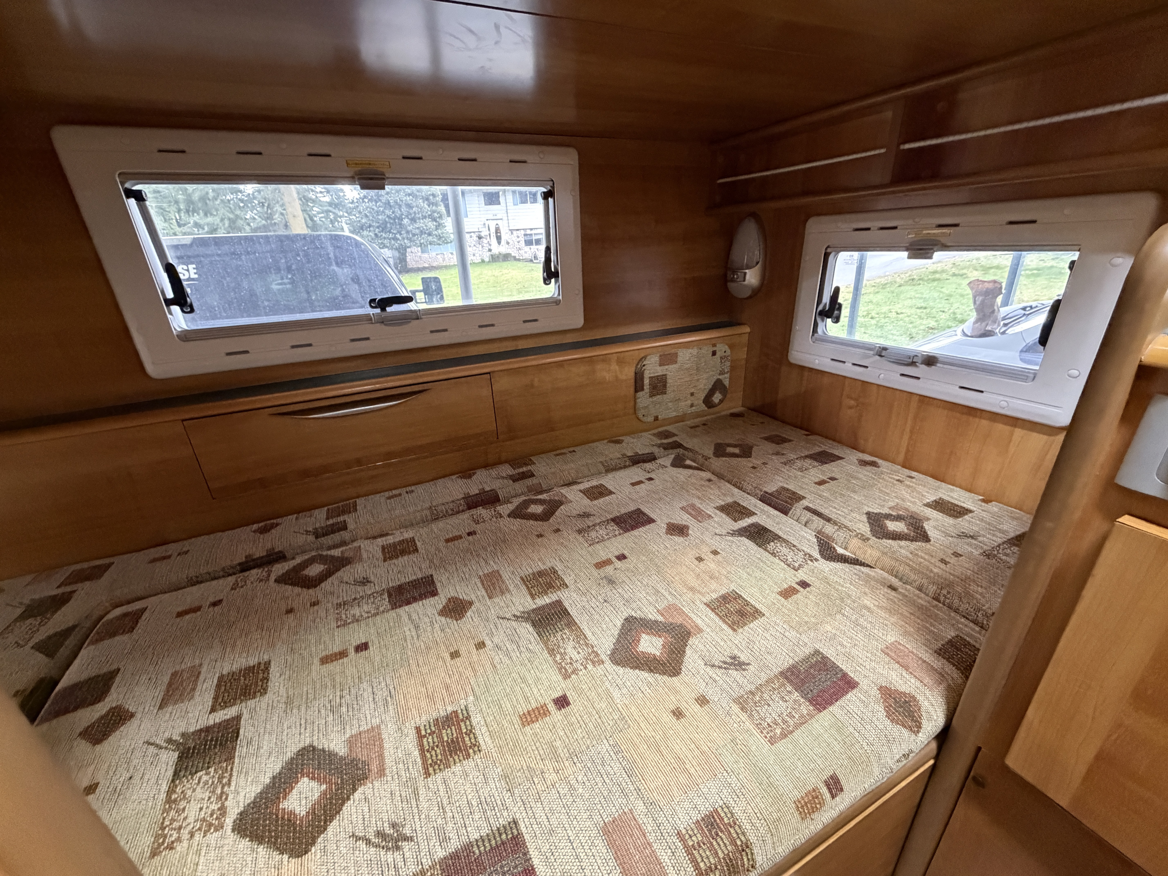 Cozy rv rental interior featuring a patterned bed, light wood walls, and natural light streaming through two bright windows.. Toyota Camroad 2005