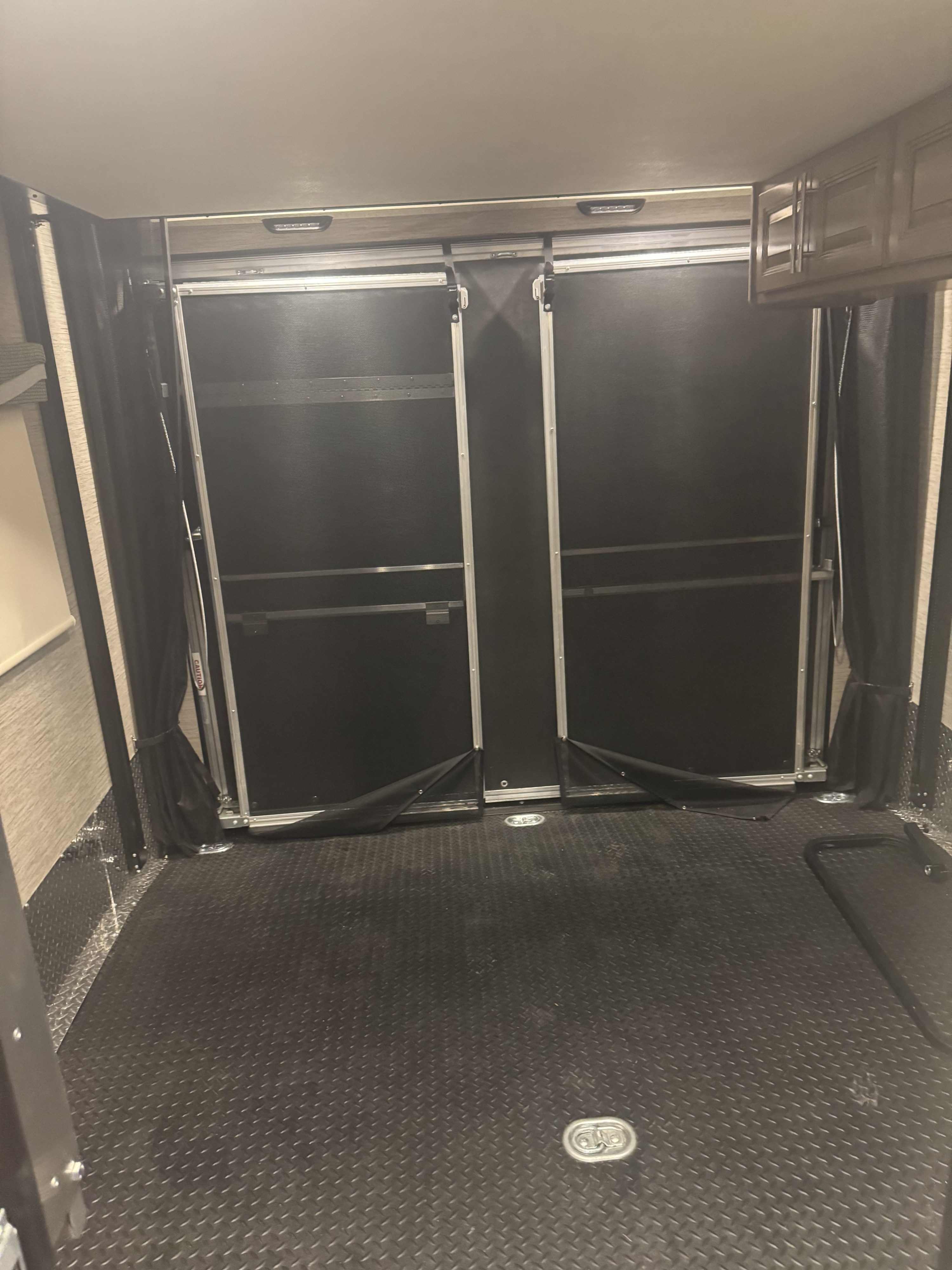 This RV rental's toy hauler interior features a rugged diamond plate floor, rear ramp doors, and tied-back mesh curtains, ideal for gear.. Thor Outlaw 2021