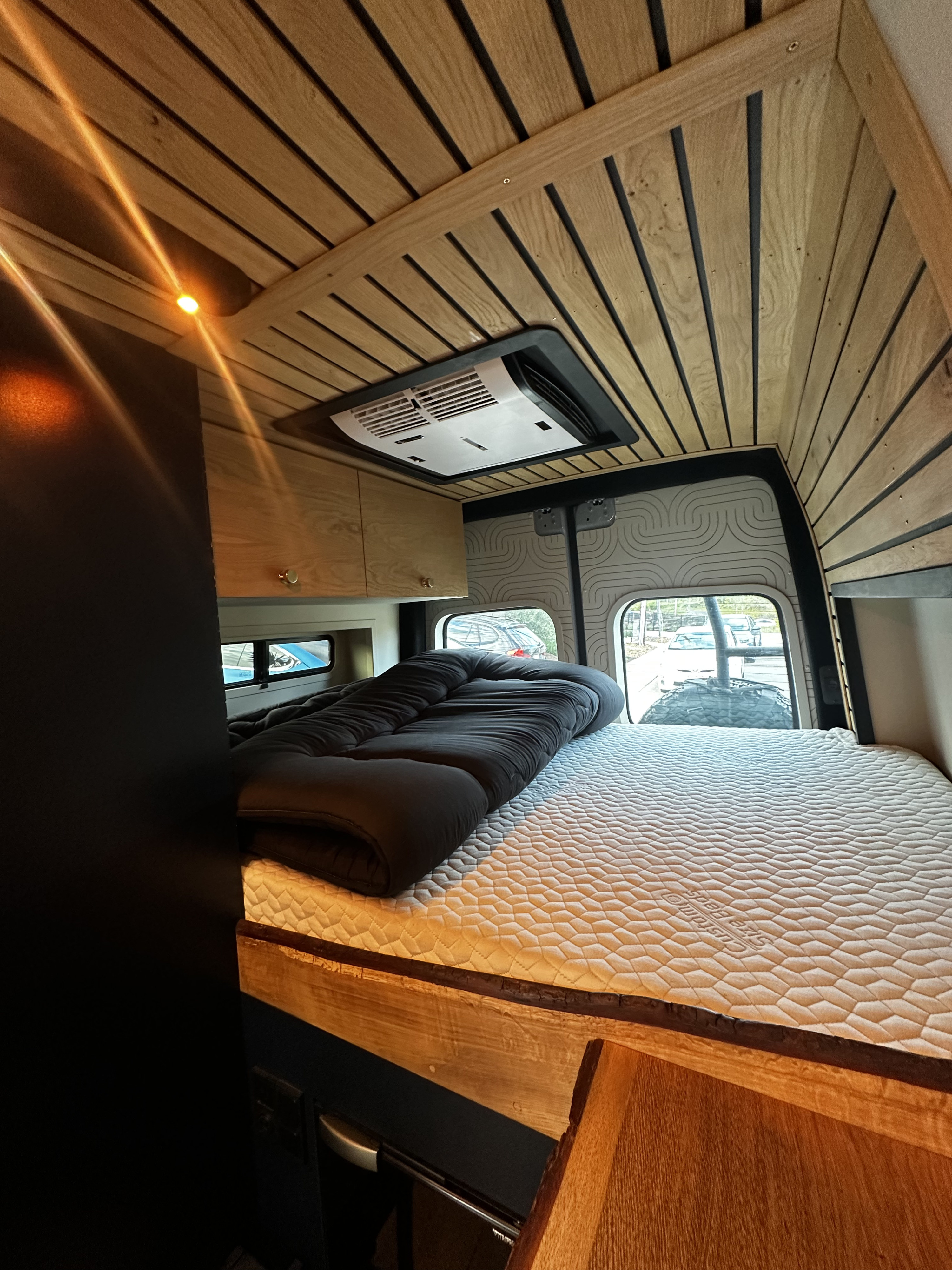 RV rental interior: A cozy bedroom featuring a slatted wooden ceiling, overhead AC, and a comfy quilted mattress.. Mercedes Sprinter 2023