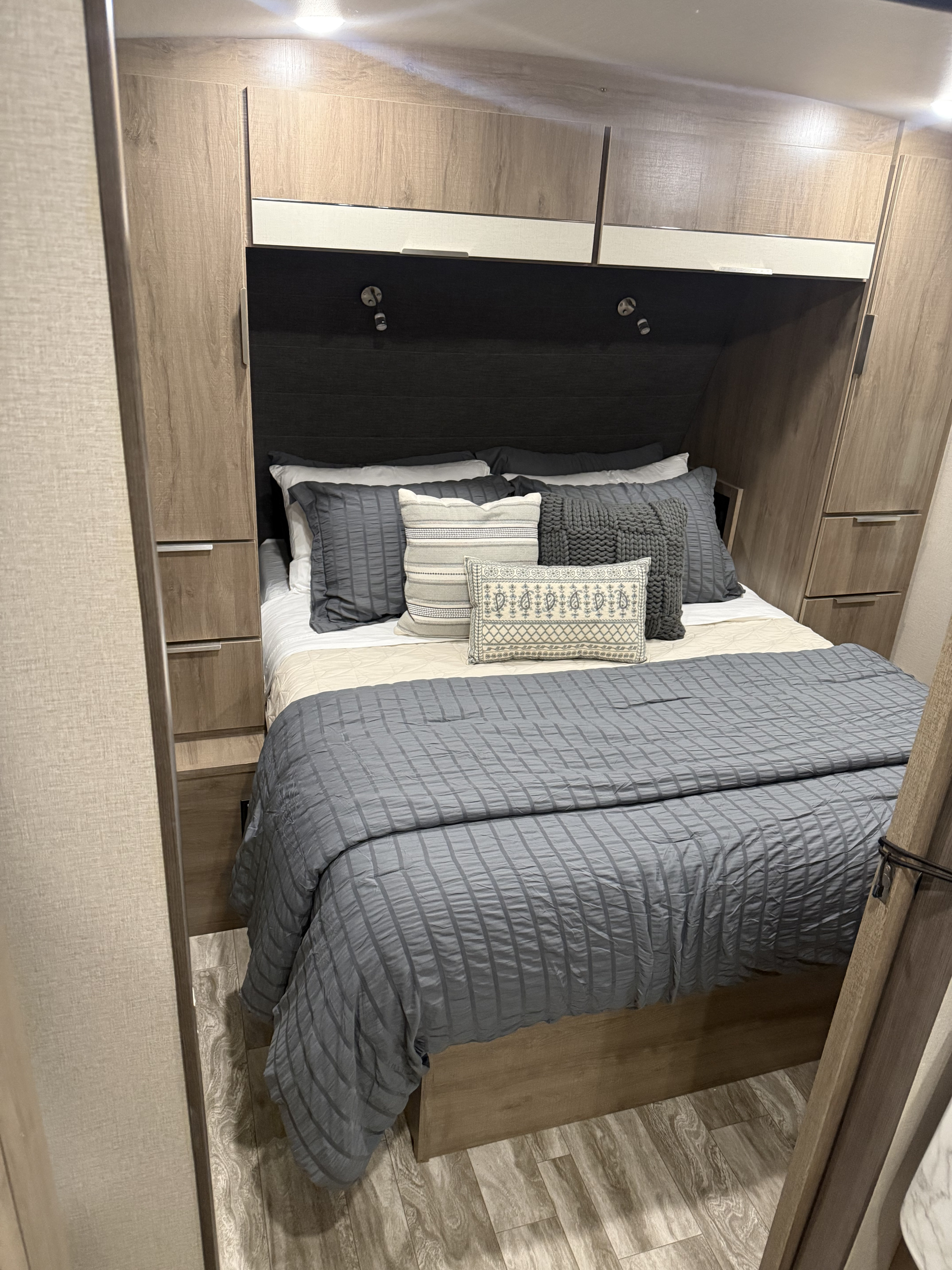 Cozy RV rental bedroom with a gray bed, decorative pillows, and wood-toned built-in storage on both sides.. Grand Design Imagine 2022