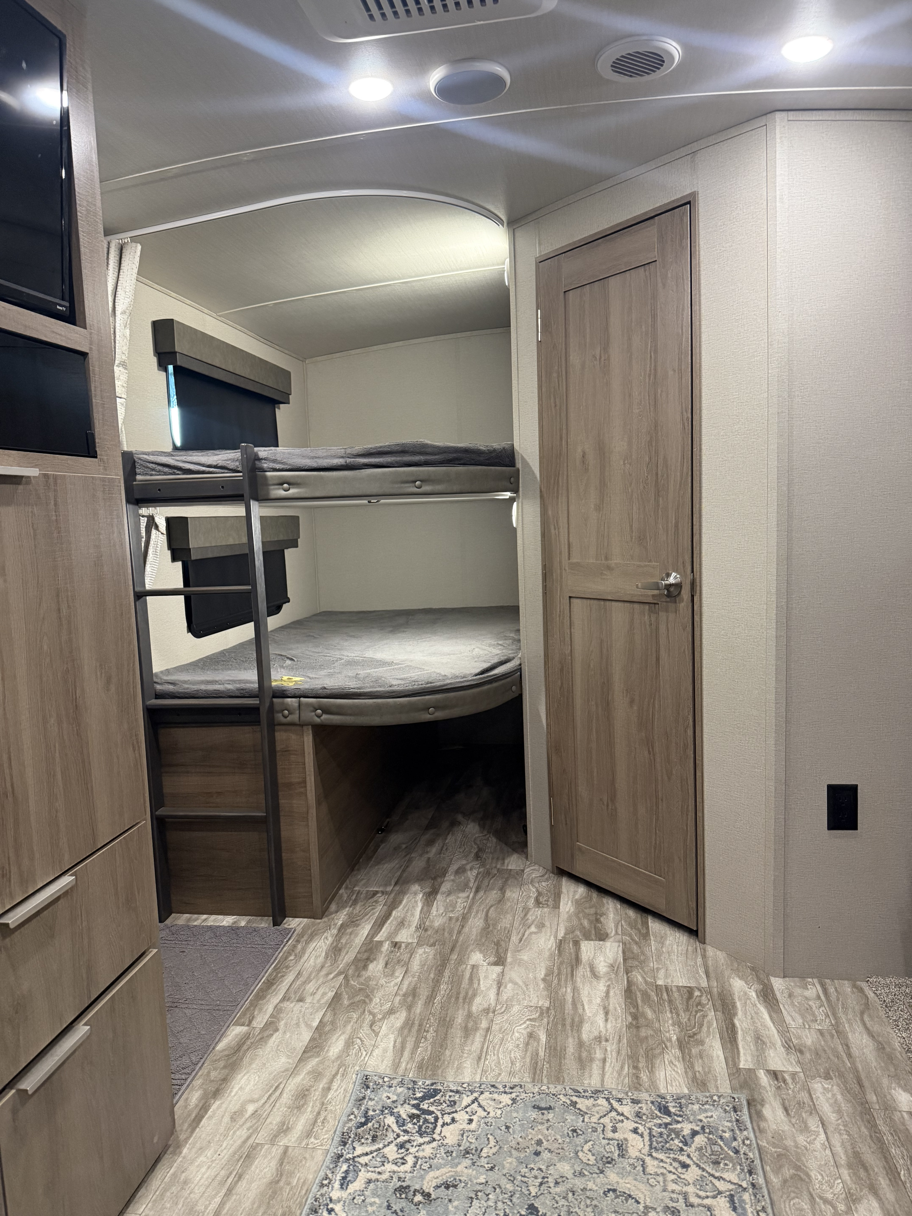 Cozy RV rental interior with modern bunk beds, a wall-mounted TV, and light wood-look flooring, offering comfort for camper families.. Grand Design Imagine 2022