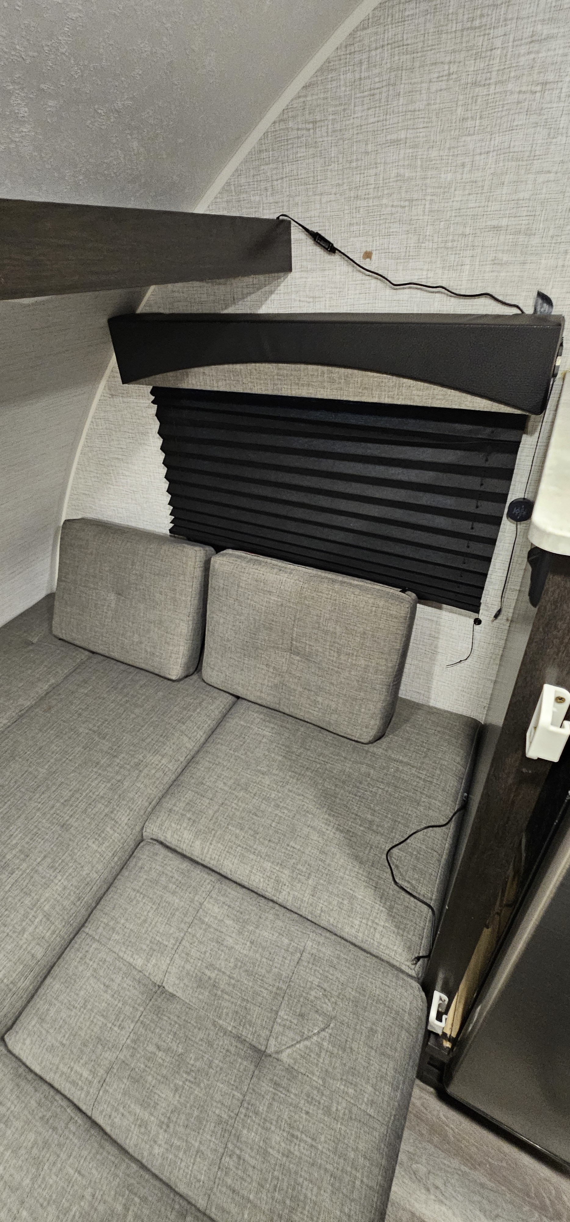 RV rental interior: View of convertible gray seating/bed, black window blind, and wall texture in a compact camper.. Braxton Creek Bushwhacker Plus 2022
