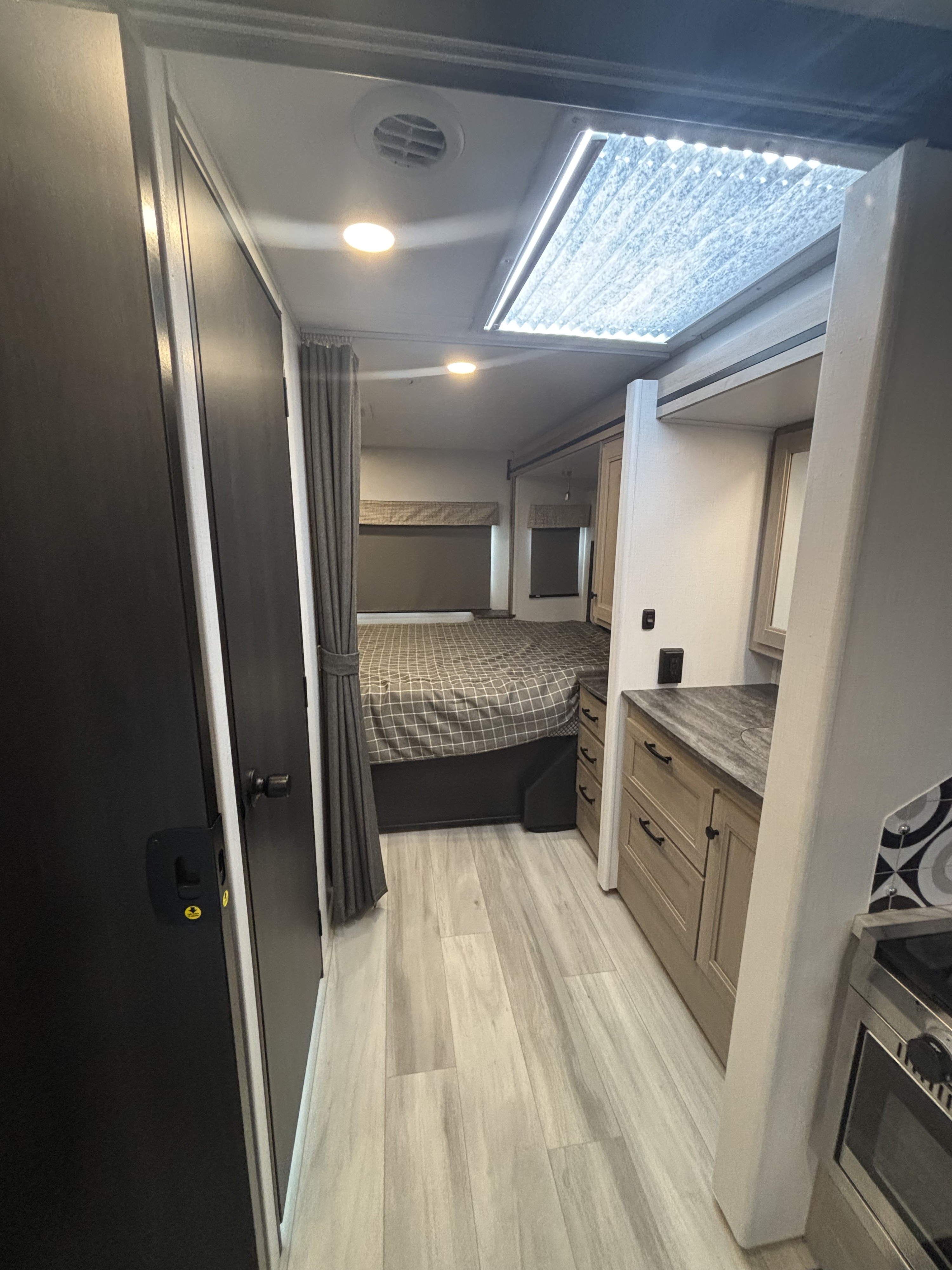 RV rental: Interior view showing a bedroom with a checkered bed, adjacent vanity, dark door, and a bright ceiling skylight.. Forest River Sunseeker Classic 2025