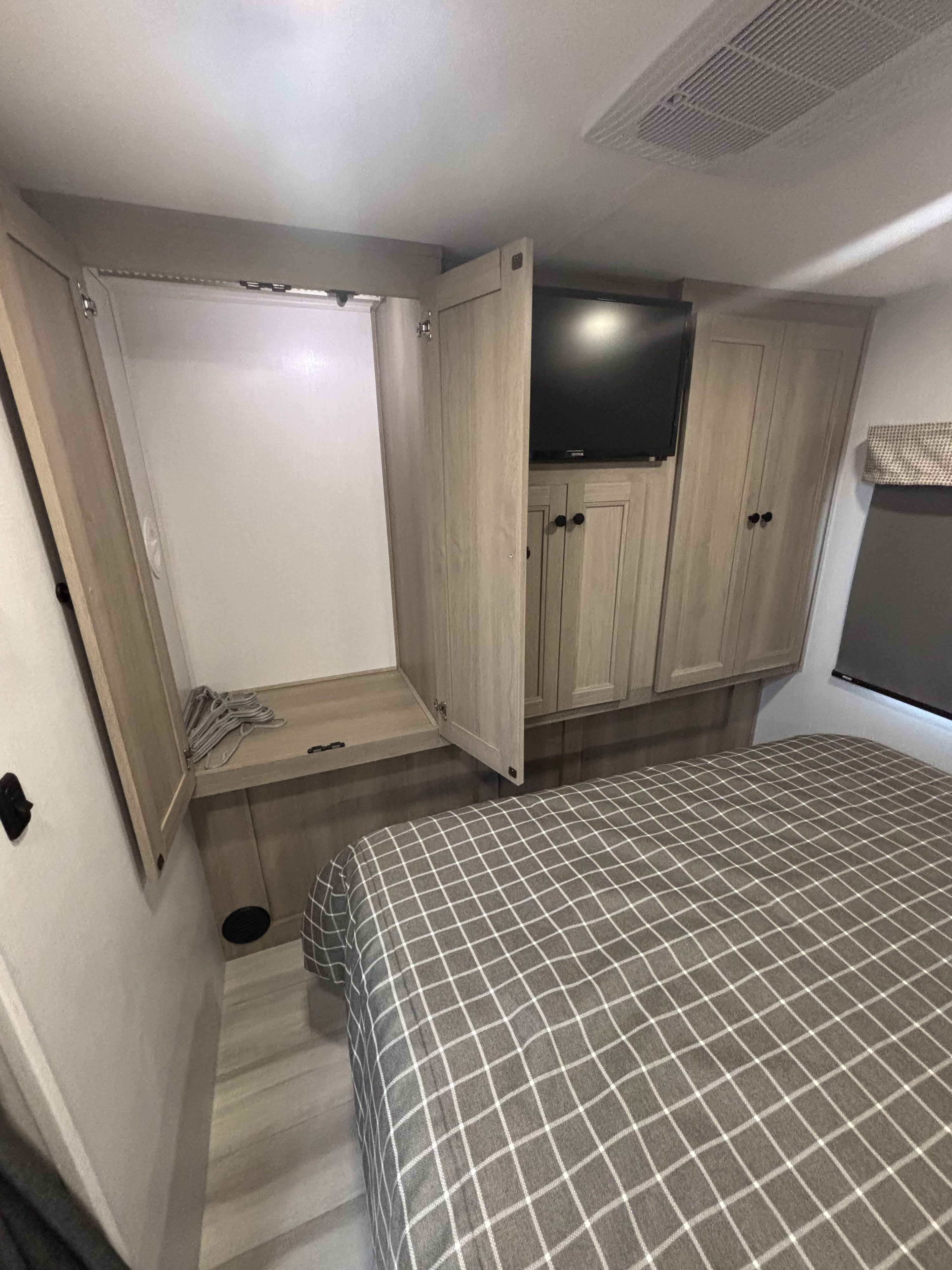 Cozy RV rental bedroom features an open closet with hangers, overhead storage, TV, and a checkered bed.. Forest River Sunseeker Classic 2025