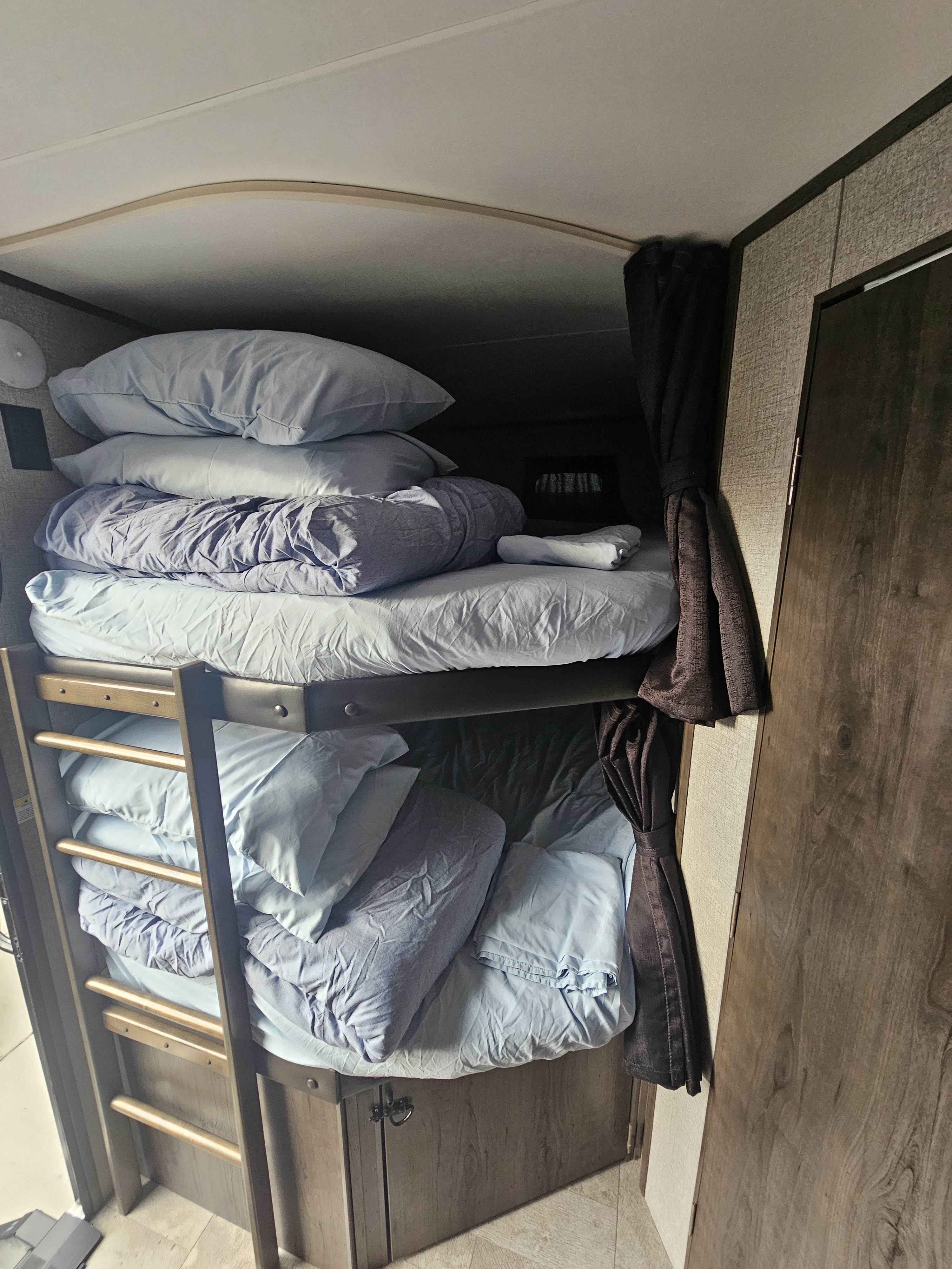 Cozy RV rental bunk beds, stacked with light blue pillows and blankets, featuring a ladder and privacy curtains.. Jayco Jay Flight 2020
