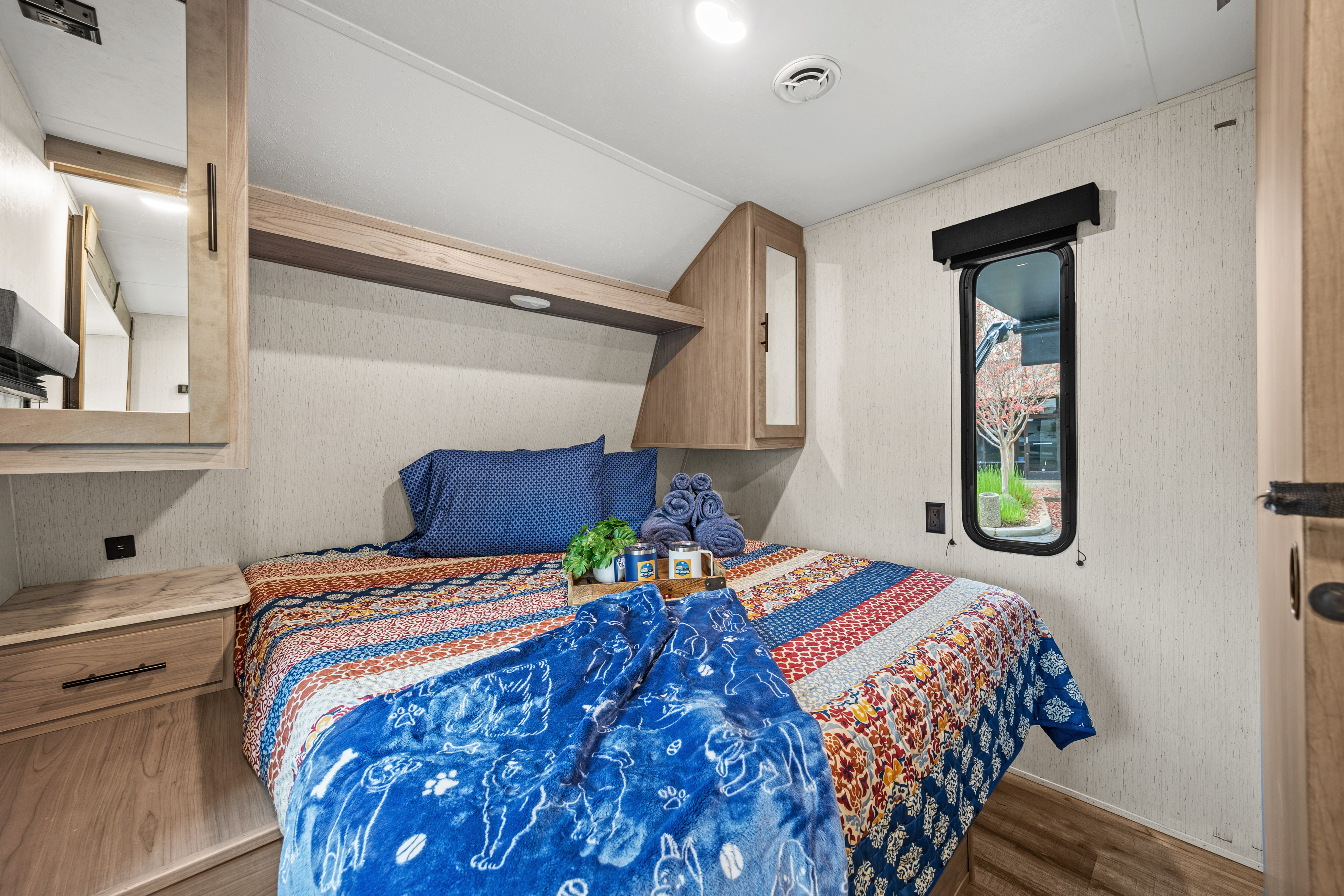 Inviting RV rental bedroom with colorful bedding, built-in storage, and a window view, offering comfort for your travels.. Coleman Lantern 2022