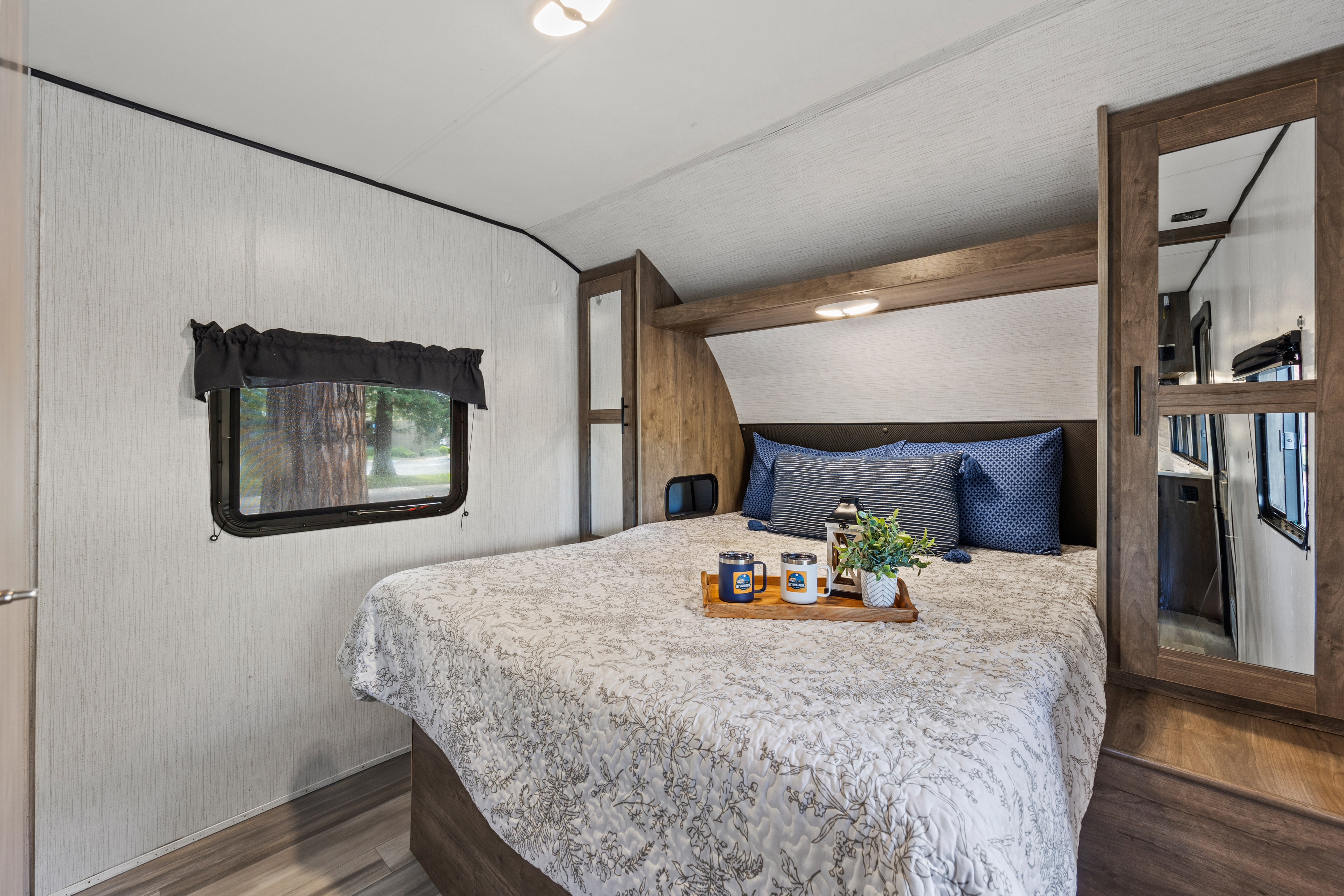 Inside a comfortable RV rental bedroom, featuring a queen bed with pillows, window view, and compact cabinetry.. Heartland RVs Pioneer 2021