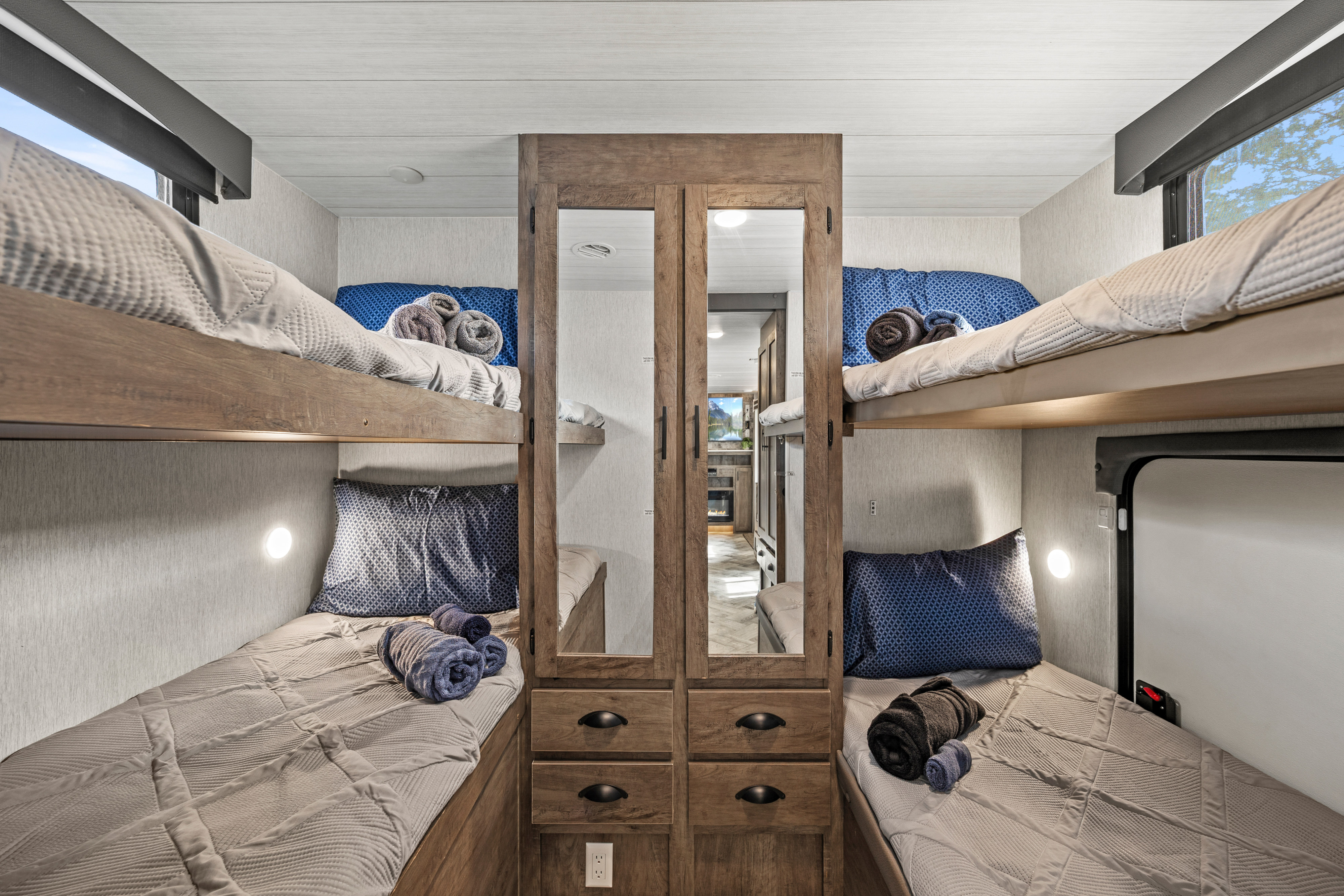 Dedicated bunk room in this RV rental: four beds with bedding, pillows, towels, lighting, and a central mirrored storage cabinet.. Forest River EVO CSJT2990 2022