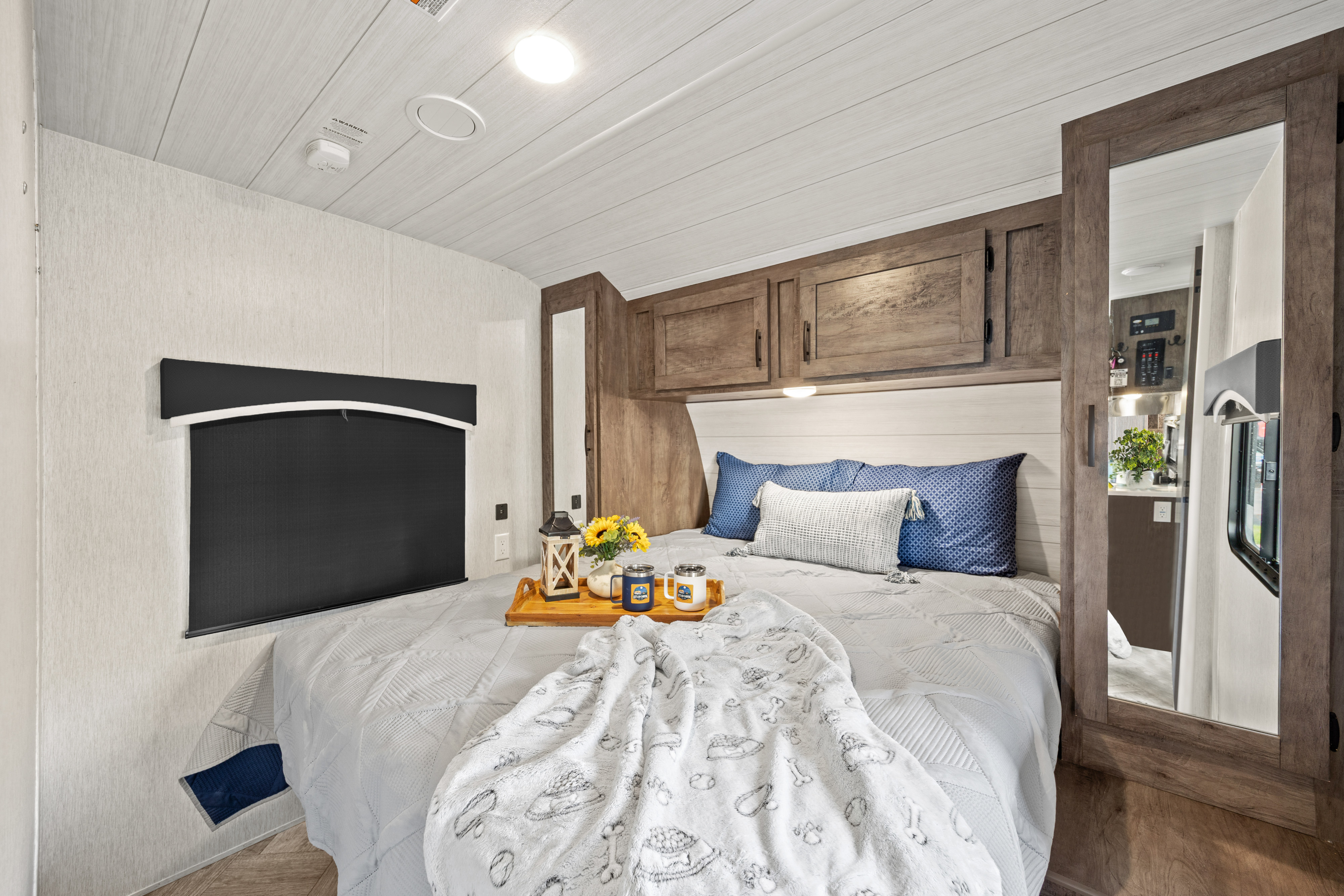 Cozy rv rental bedroom featuring a comfortable bed, blue pillows, overhead wood cabinets, and a side mirror.. Forest River EVO CSJT2990 2022
