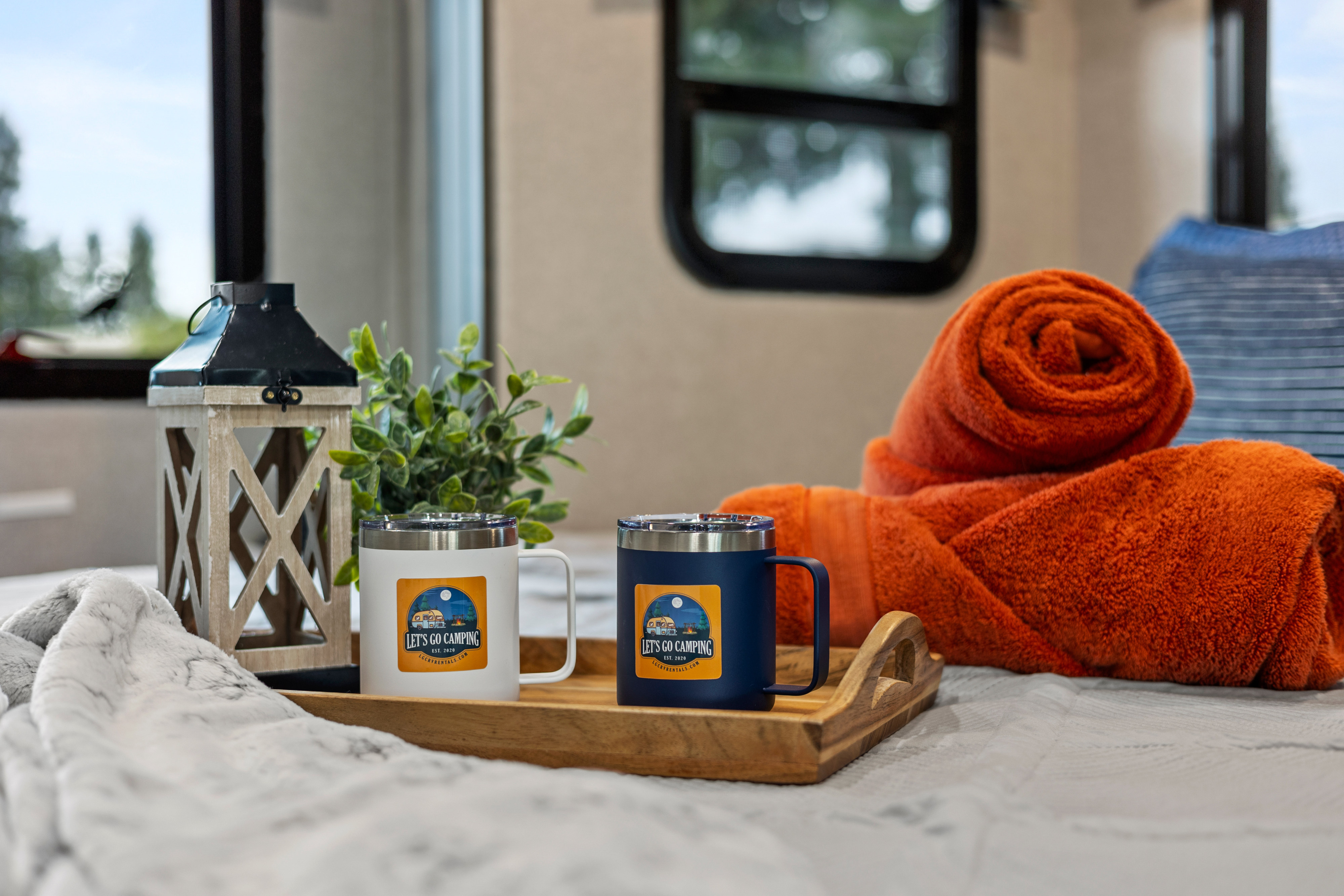 Cozy RV rental interior with "Let's Go Camping" mugs, a wooden lantern, and soft blankets on a wooden tray.. Dynamax Corp Isata 2021