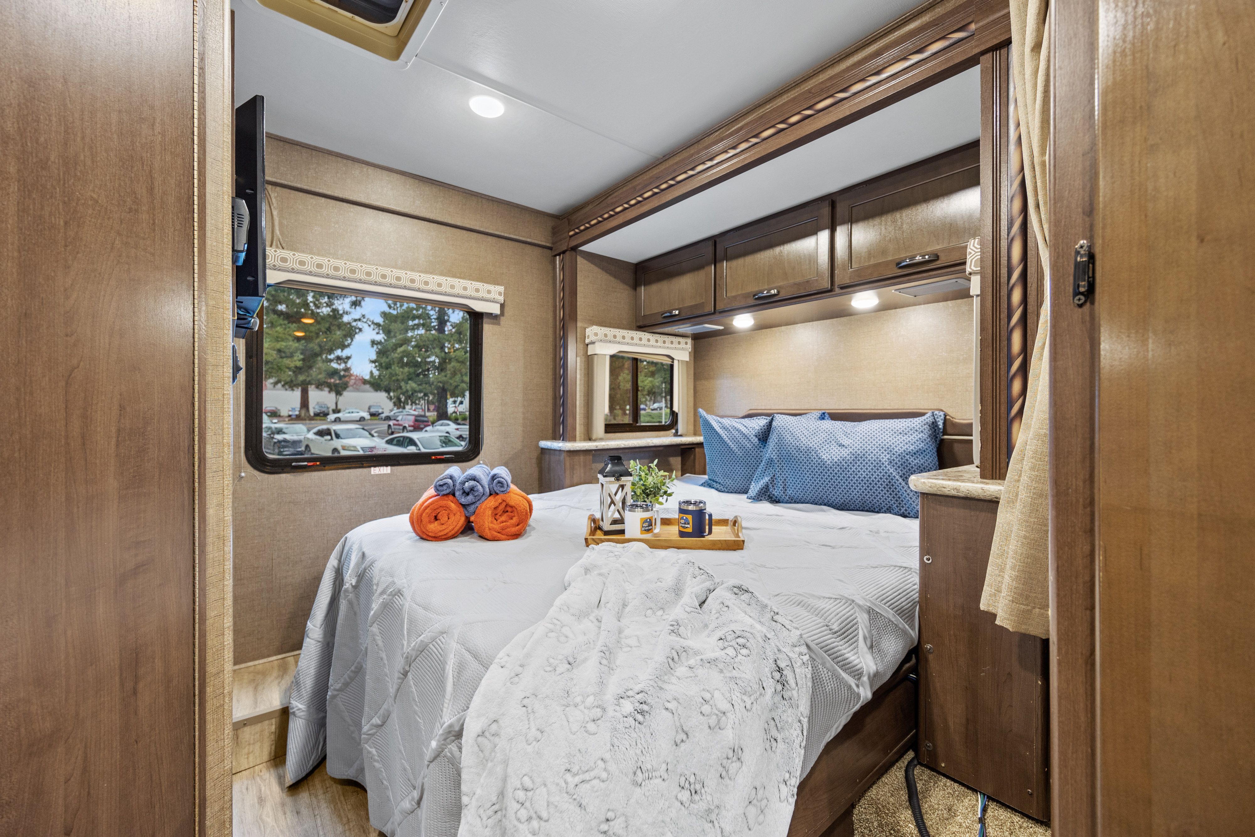 Cozy rv rental bedroom featuring a comfy bed, pet-friendly blanket, overhead storage, and a window view.. Thor Four Winds 2017