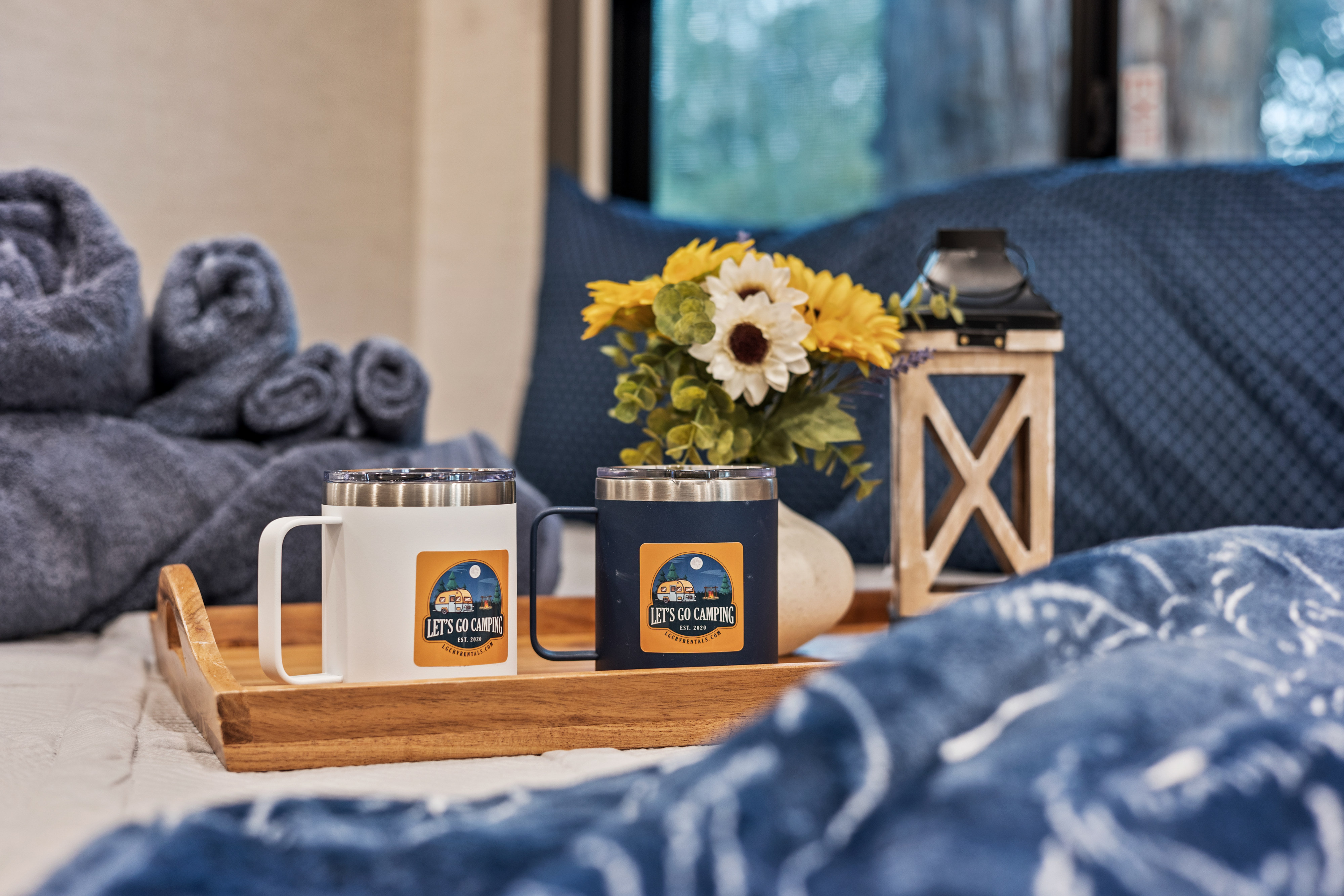 Cozy rv rental ambiance featuring branded "Let's Go Camping" mugs, fresh flowers, and rolled towels on a wooden tray.. Thor Freedom Elite 2025