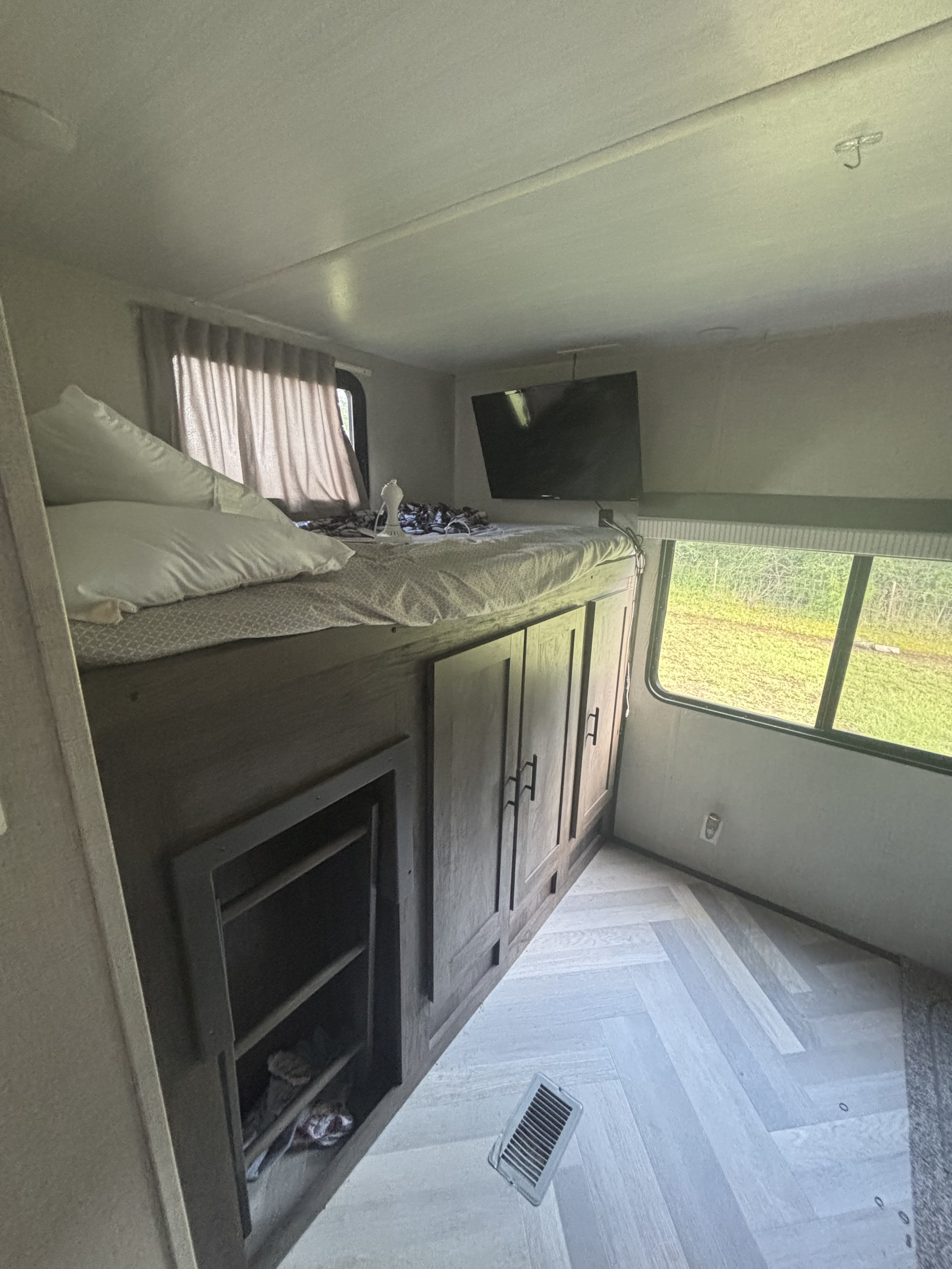 Cozy rv rental bunk room: elevated bed, storage cabinets, wall-mounted TV, window view, and light herringbone floor.. Forest River Salem 2021