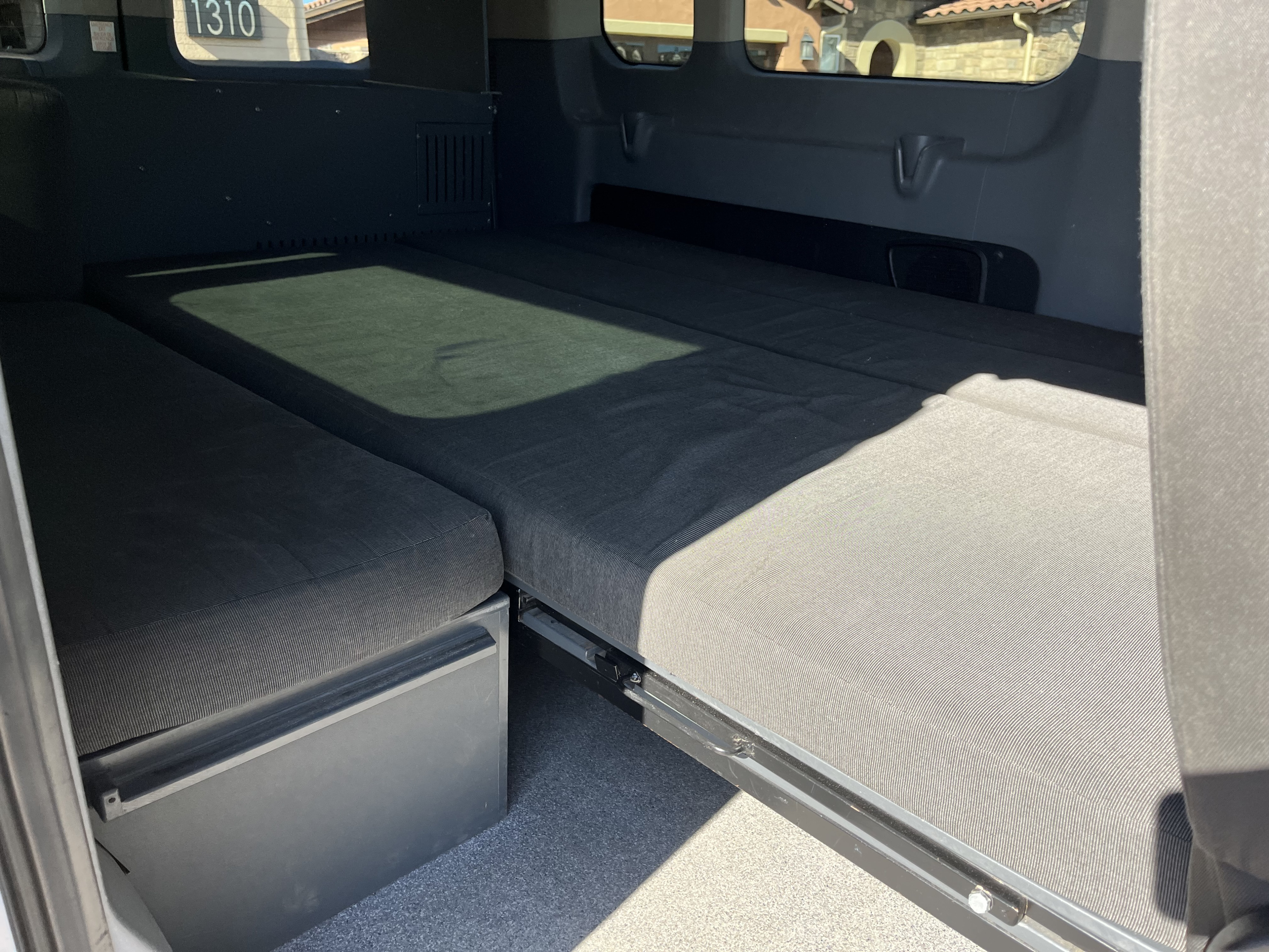 RV rental camper van interior featuring a modular gray upholstered bed, with sections extended, ideal for sleeping.. Ford Custom Transit 2017