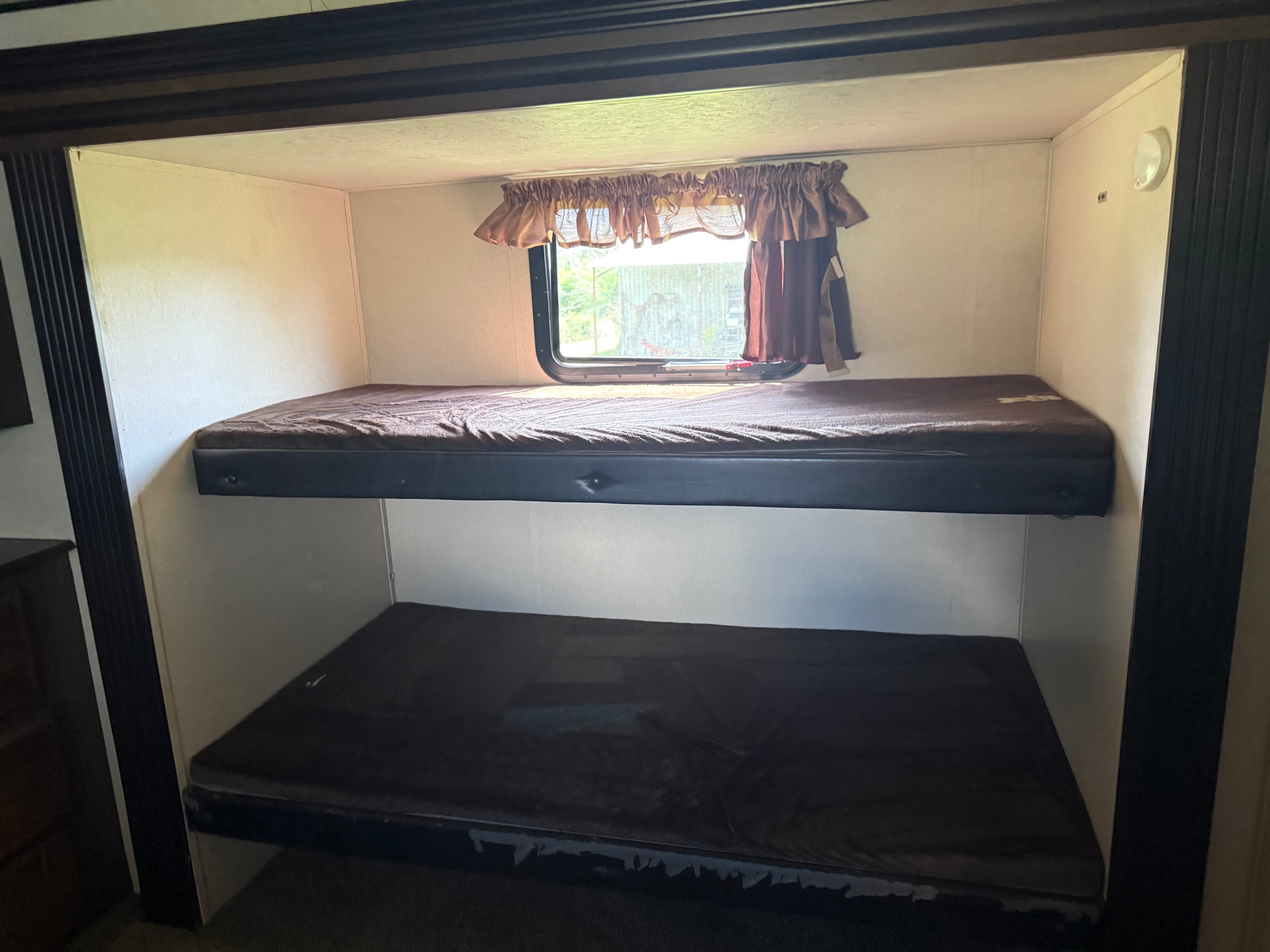 RV rental: Two bunk beds with brown mattresses inside a compact sleeping area. Window with curtains and a light fixture.. Forest River Wildwood Heritage Glen Lite 2018