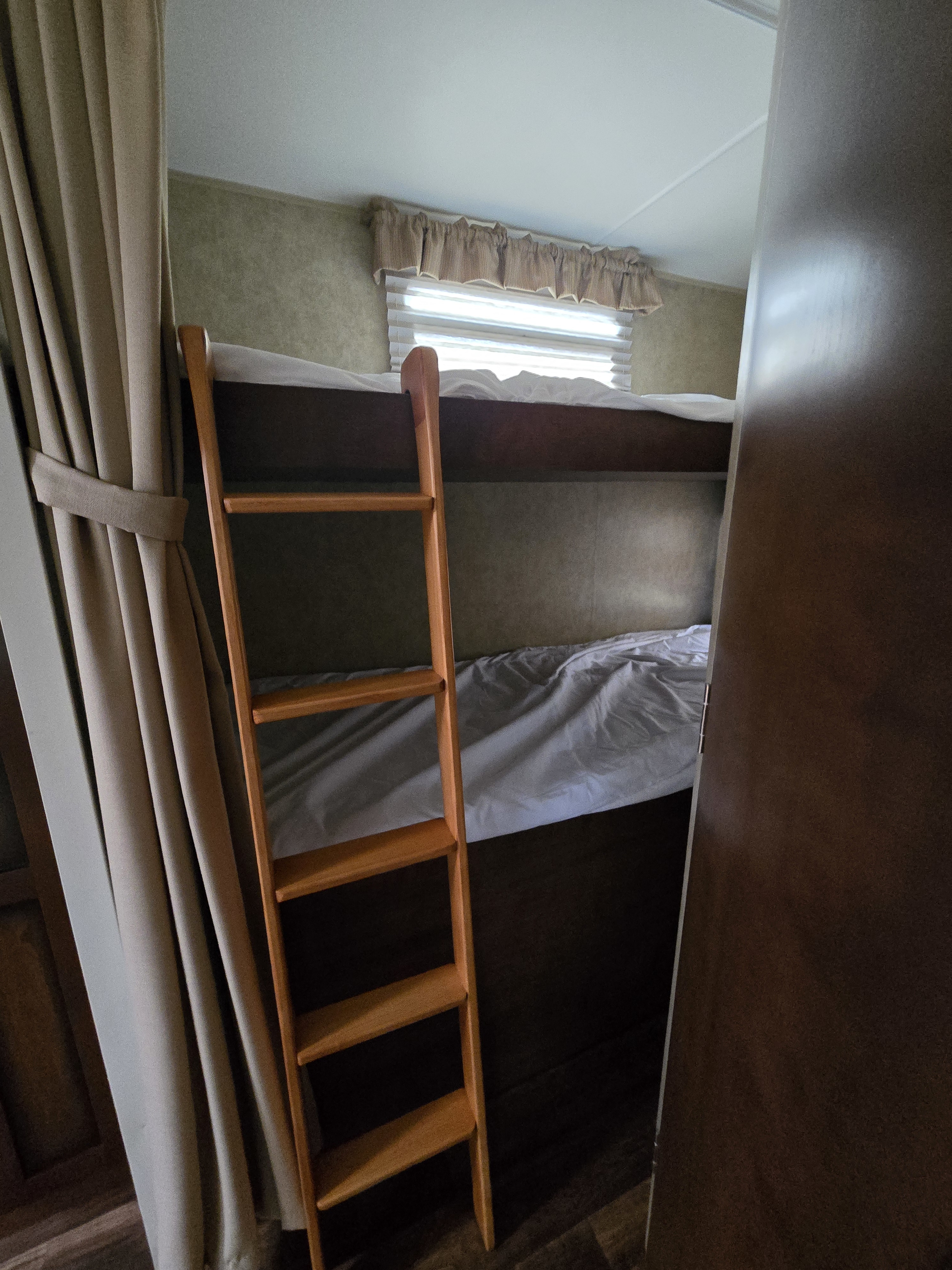 This RV rental features practical bunk beds with a wooden ladder, window, and privacy curtains, ideal for travel.. Dutchmen Kodiak Ultimate 2012