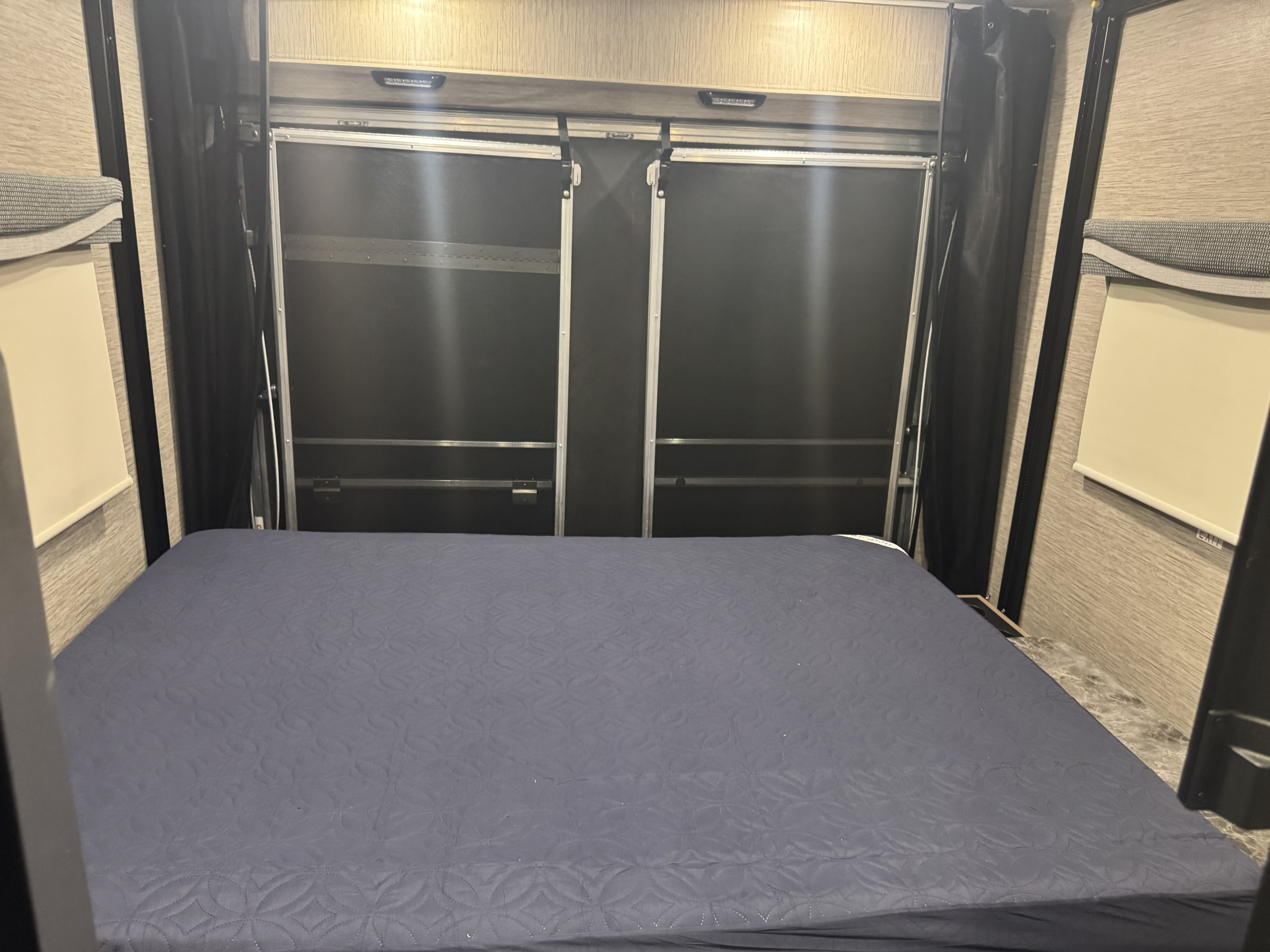 RV rental bedroom with a comfy bed at the rear garage door, flanked by black privacy curtains and side window shades.. Thor Outlaw 2021