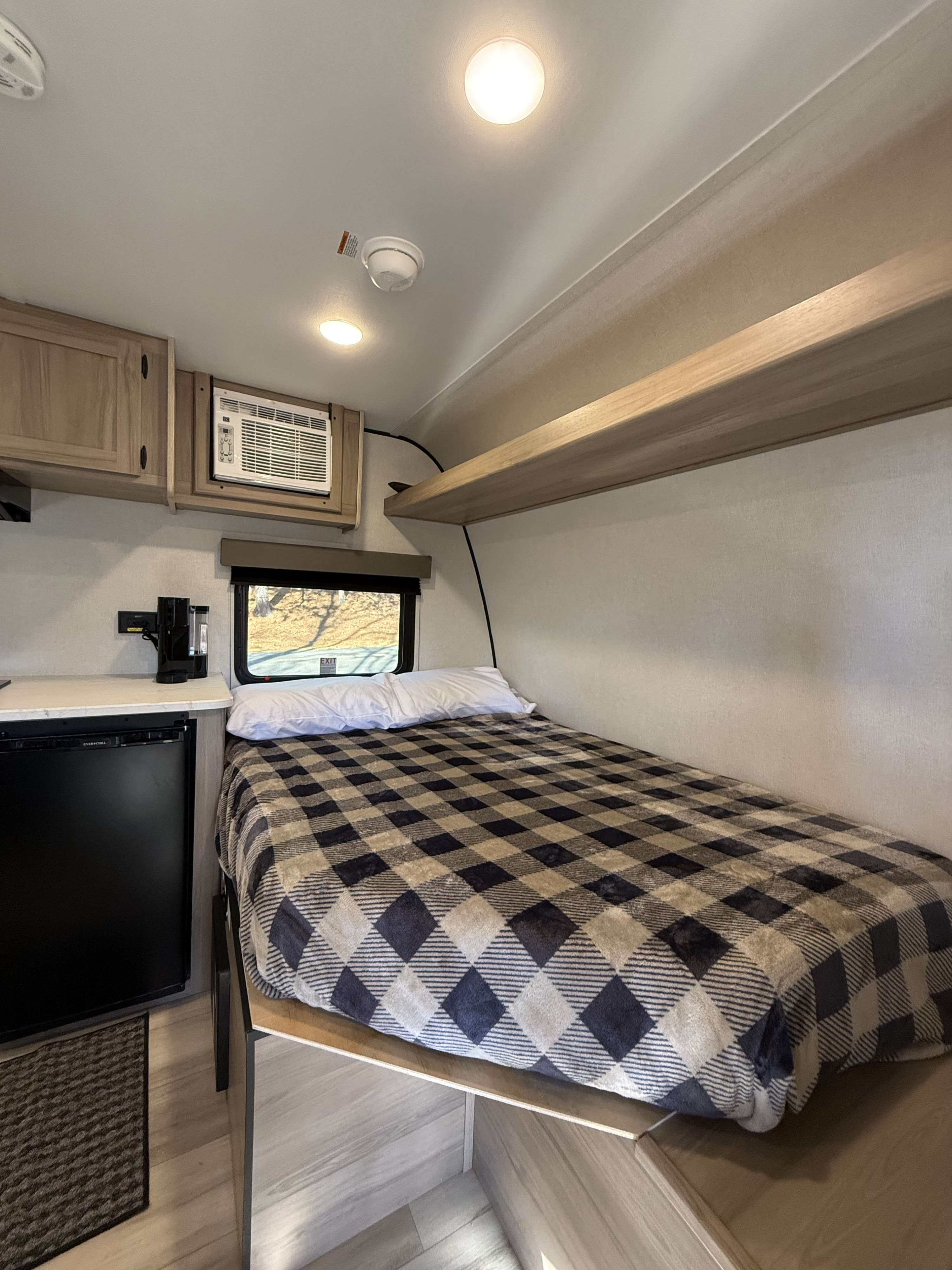Cozy RV rental bedroom featuring a checkered bed, window, AC, fridge, and overhead storage for a comfortable stay.. Keystone Coleman 13R 2026