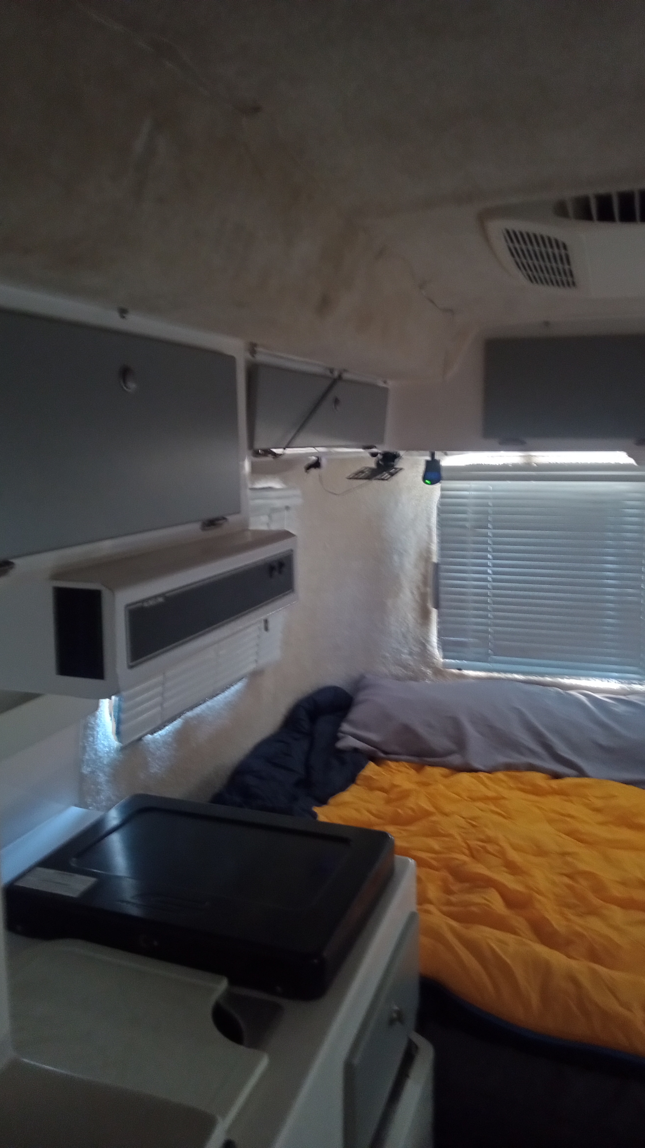 Cozy RV rental interior: bed with orange sleeping bag, window, overhead storage, and counter with electric griddle.. Casita Spirit Deluxe 2020