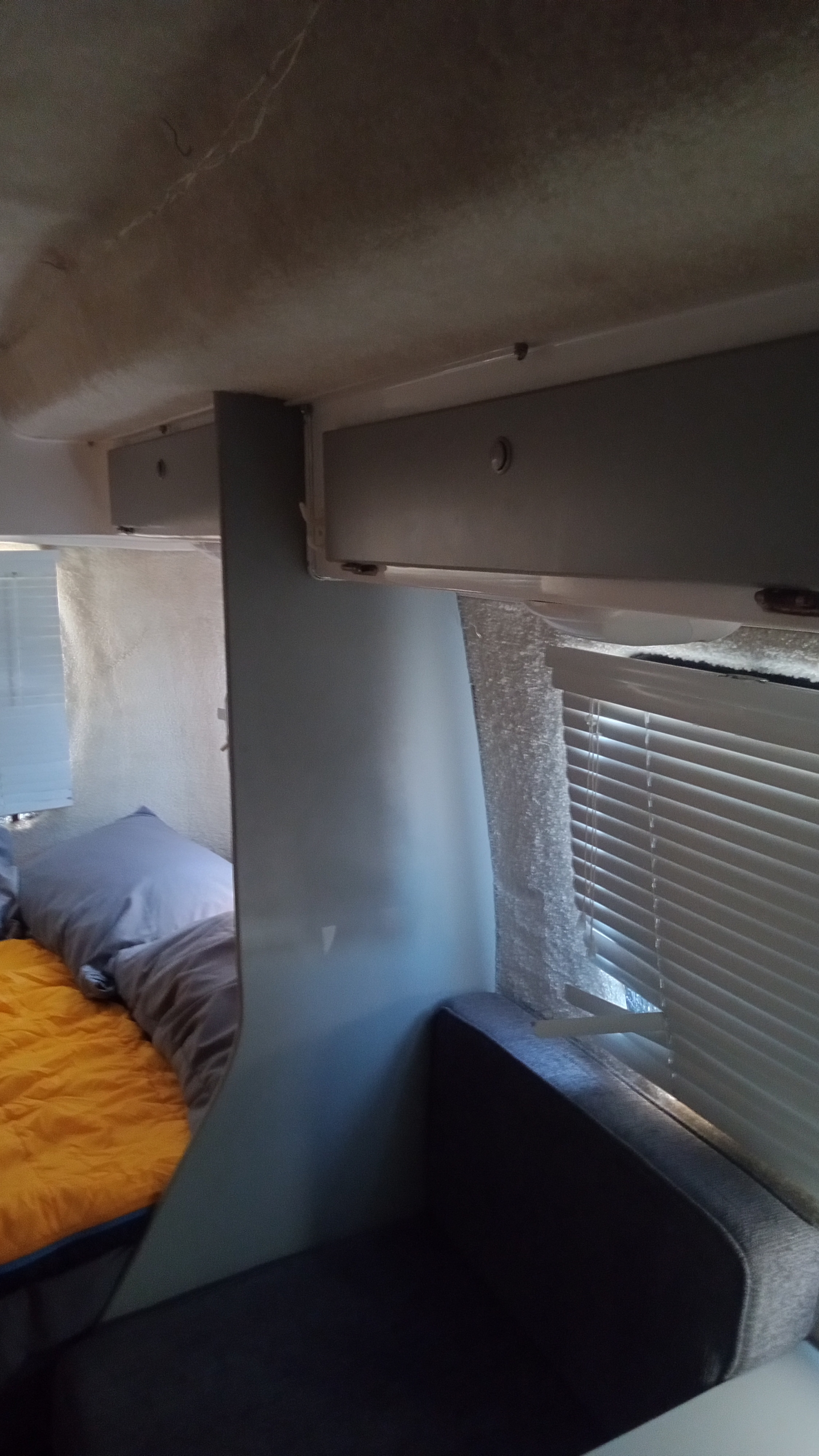 Cozy RV rental interior with a bed (orange comforter), dark upholstered seating, overhead storage, and window blinds.. Casita Spirit Deluxe 2020