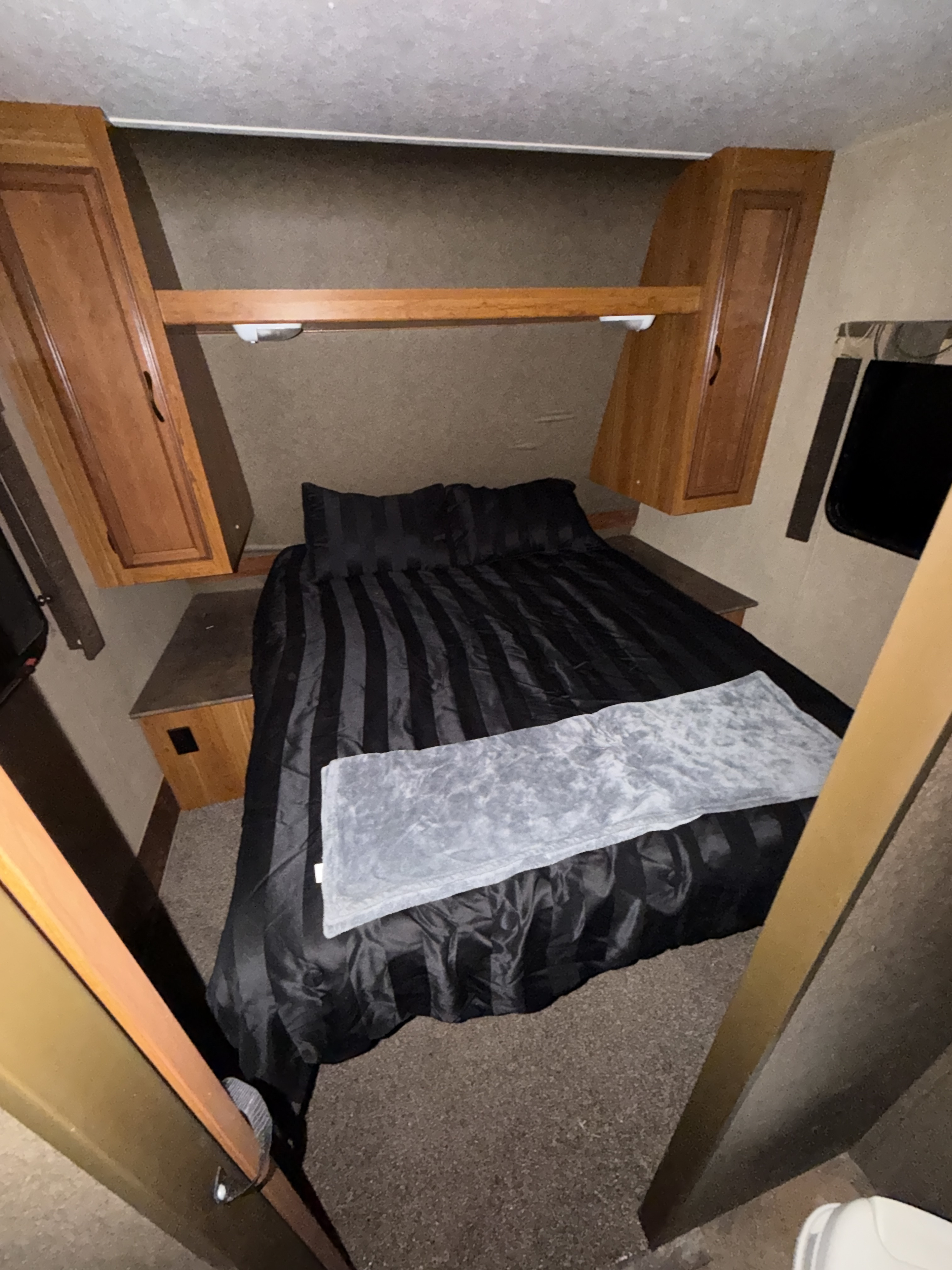 Compact RV rental bedroom featuring a bed with black striped bedding, a grey throw, and wood cabinetry.. Starcraft Launch Ultra Lite 2015
