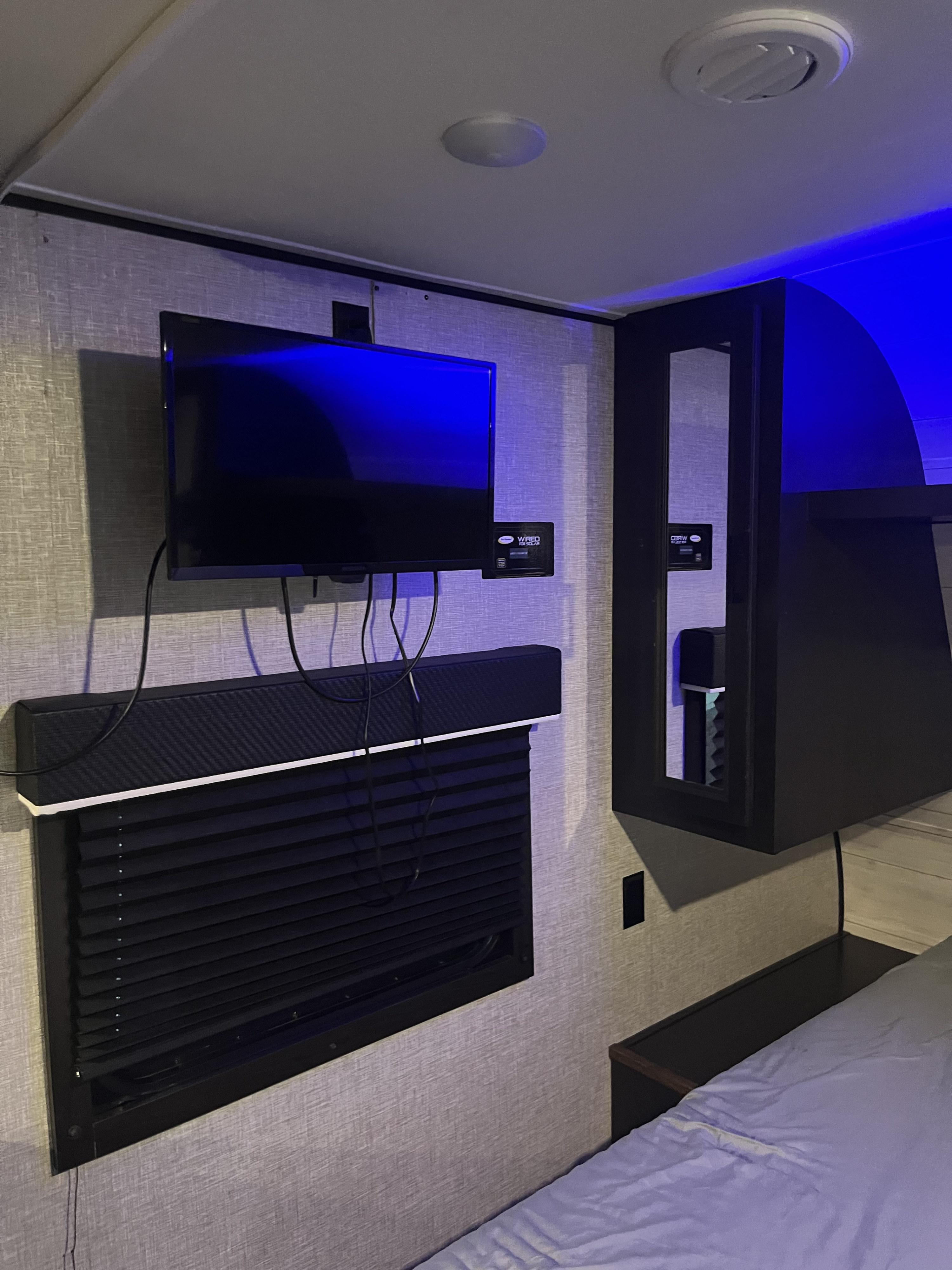 Modern RV rental bedroom with wall-mounted TV, soundbar, black blinds, and ambient blue lighting, creating a cozy and functional space.. Jayco Jay Flight SLX Rocky Mountain Edition 2022