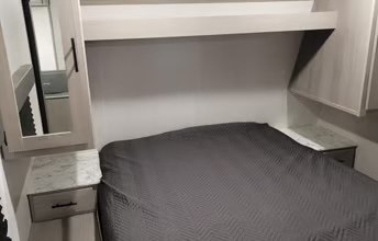 Cozy RV rental bedroom features a dark gray bed, nightstands, and overhead cabinets for comfortable travel.. Dutchmen Coleman Lantern 2022