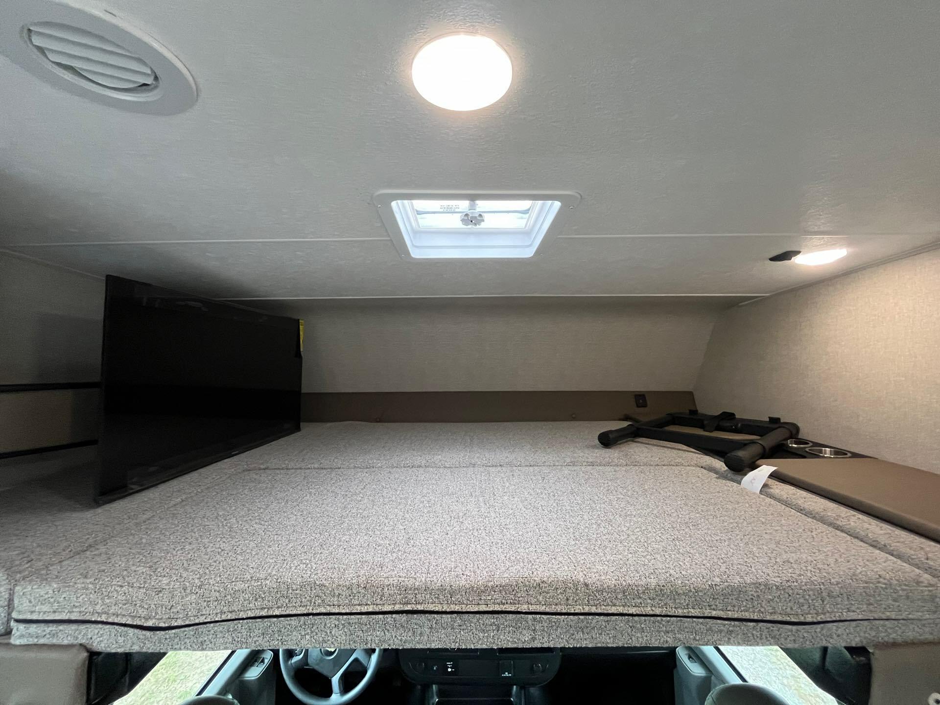 Inside an RV rental: a comfortable cab-over bunk bed with a TV and ceiling vent/light, offering extra sleeping space.. Forest River Coachmen Freelander 2025